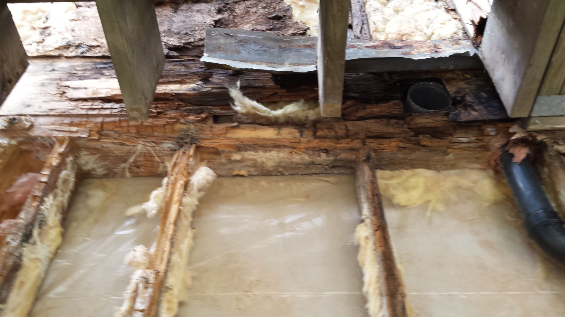 Damaged wooden floor with exposed insulation, moisture stains, and a black pipe opening