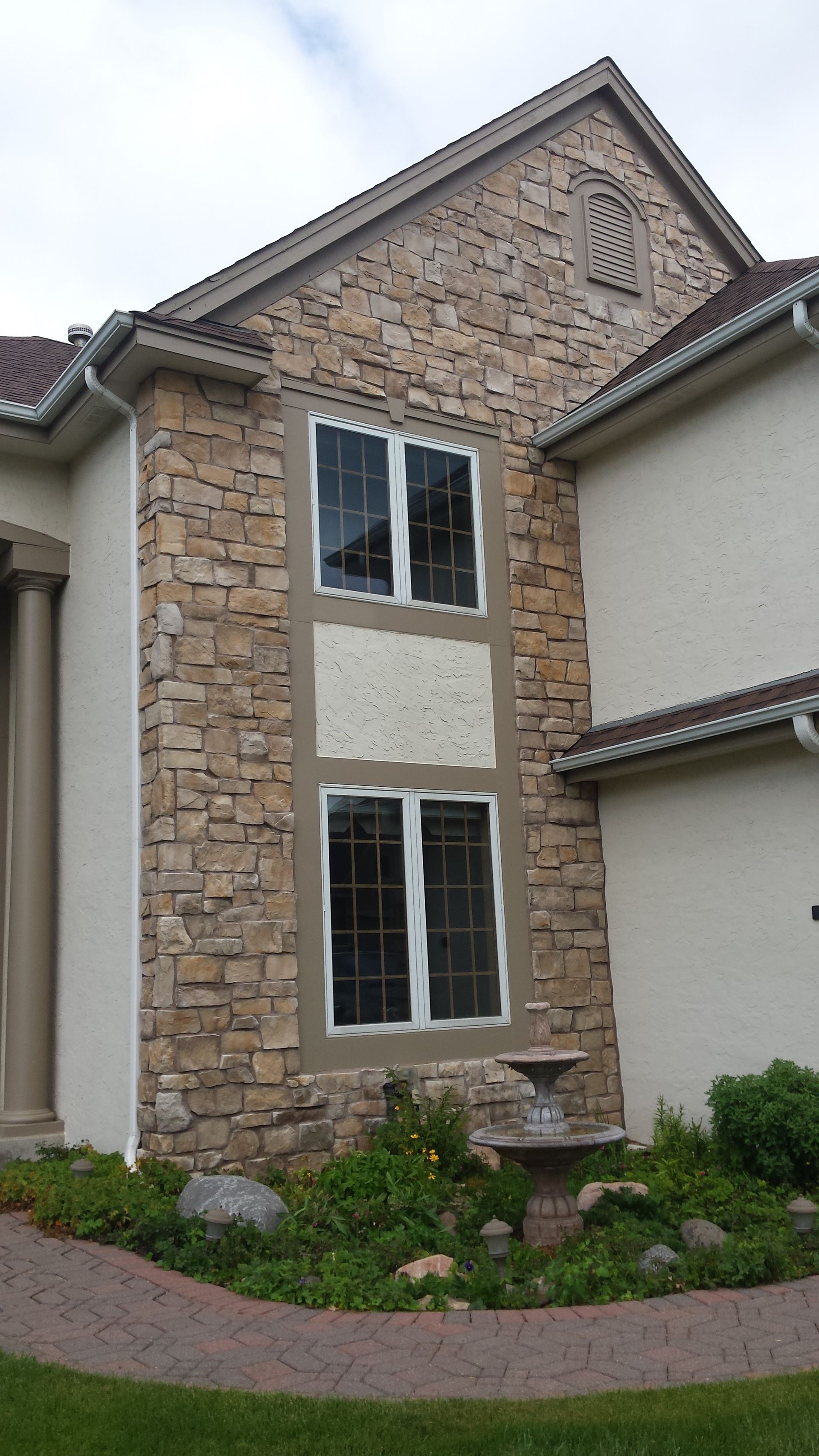 Stone townhouse facade with two windows, tan siding accents, and a landscaped front path