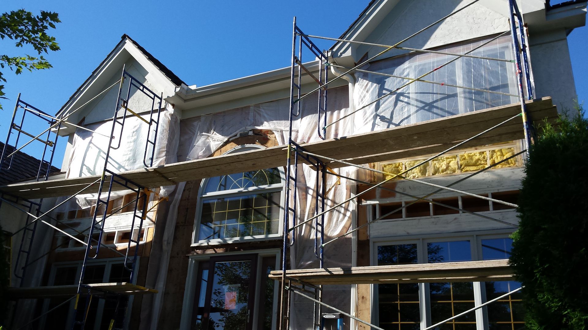 Scaffolding around a house under construction with white siding and a gray roof