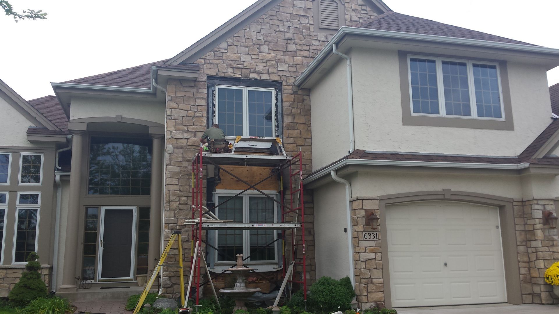 Brick suburban house with front scaffolding and ladder, under repair beside a garage.