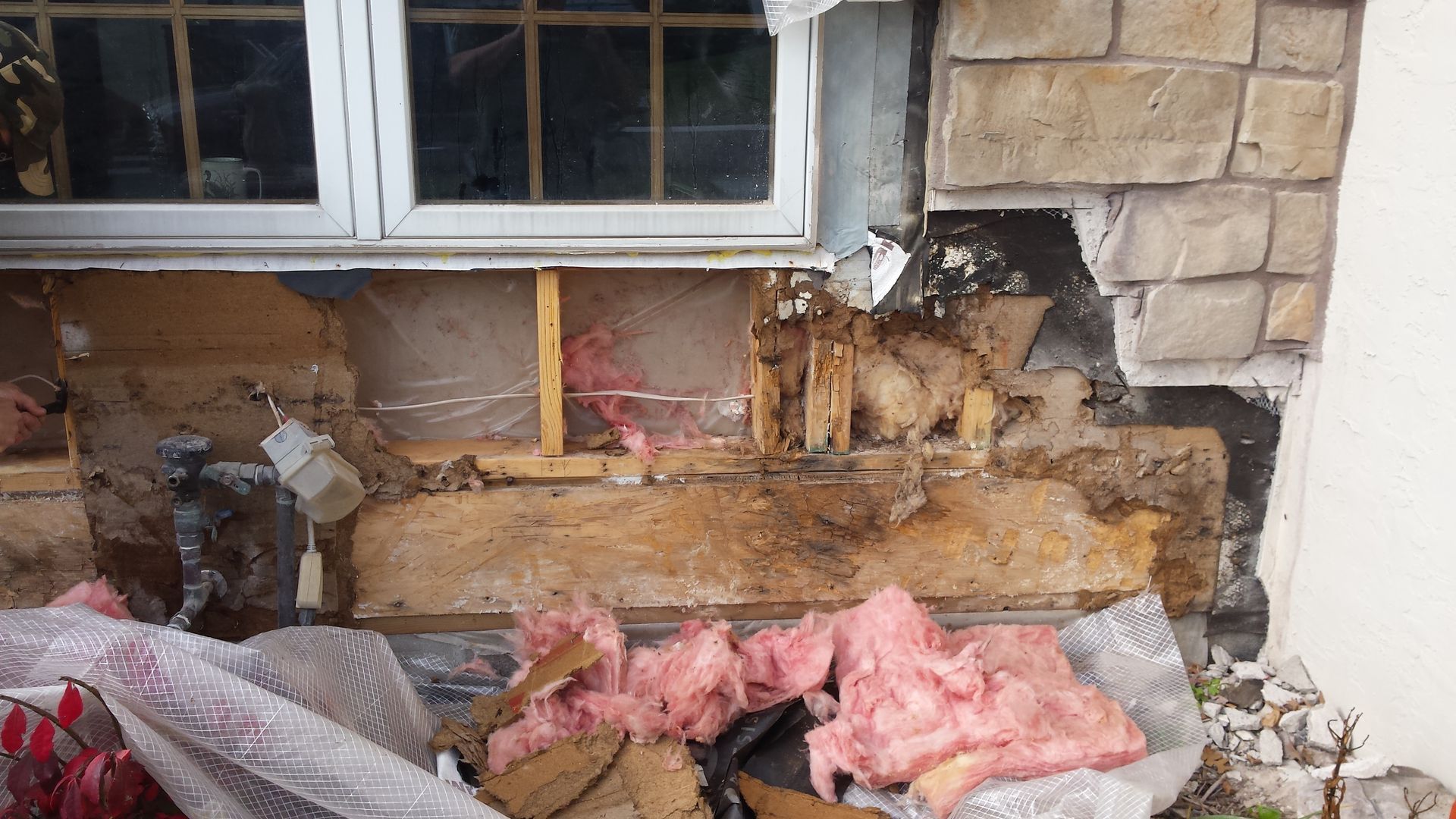 Damaged brick wall beneath a window, with insulation and debris exposed in the lower section.