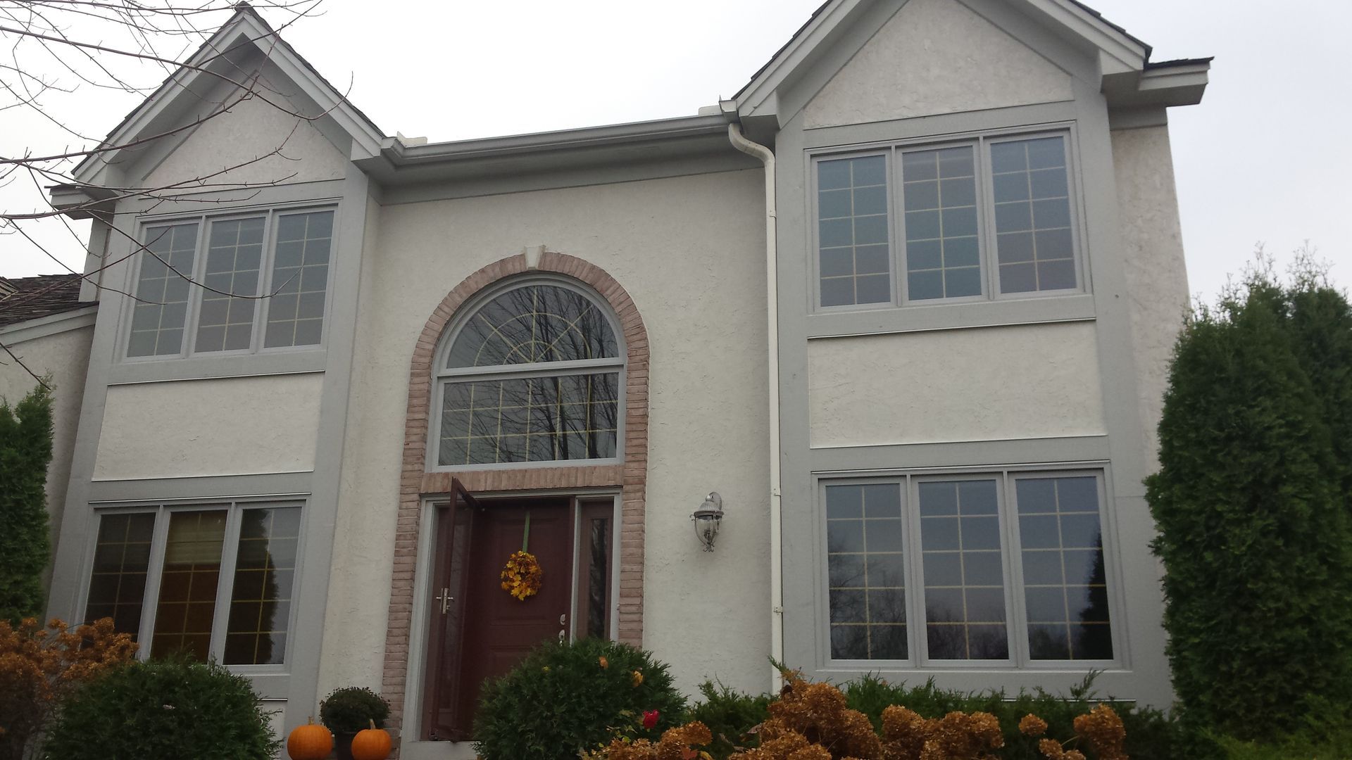 Two-story beige house with arched front window, double garage, and autumn decorations on the porch