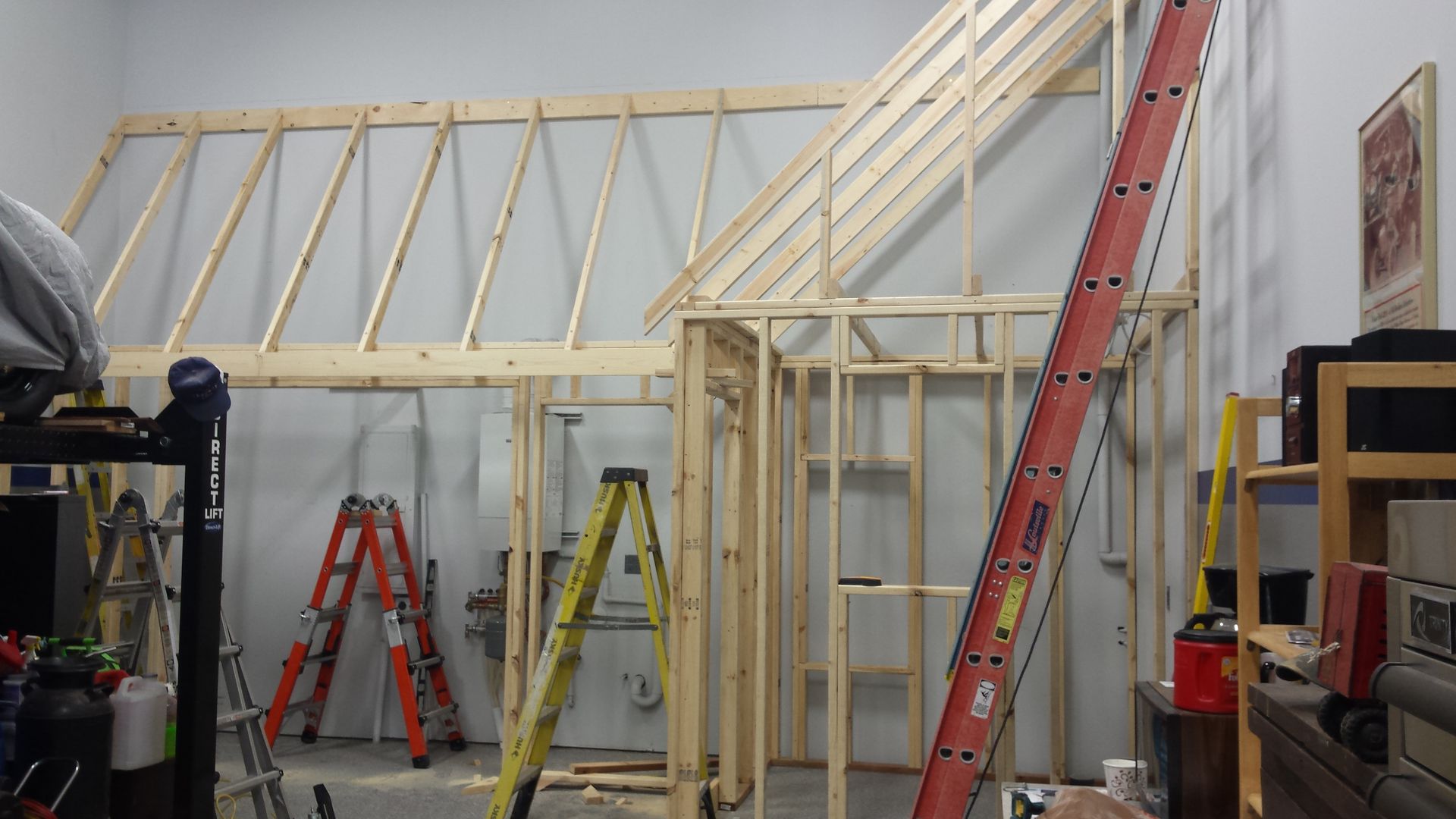 Workshop with unfinished wooden wall framing, ladders, and tools under construction.