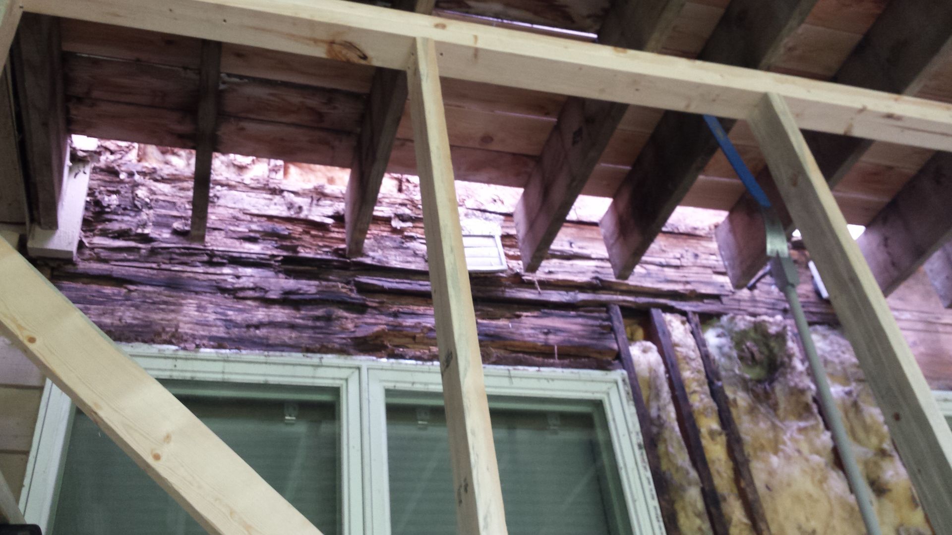 Partially demolished roof above a window, exposing damaged wood framing and insulation.