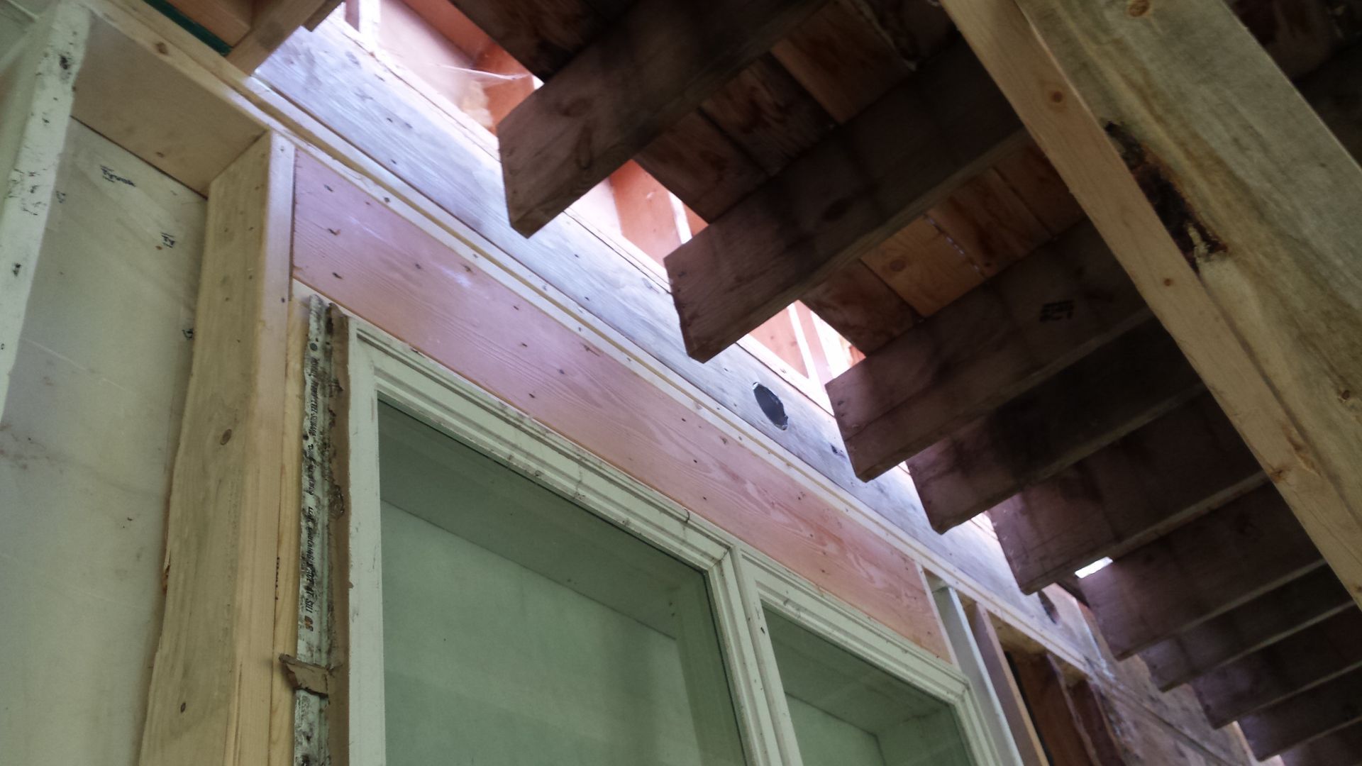 Upward view of house eaves with exposed rafters above a window and beige siding
