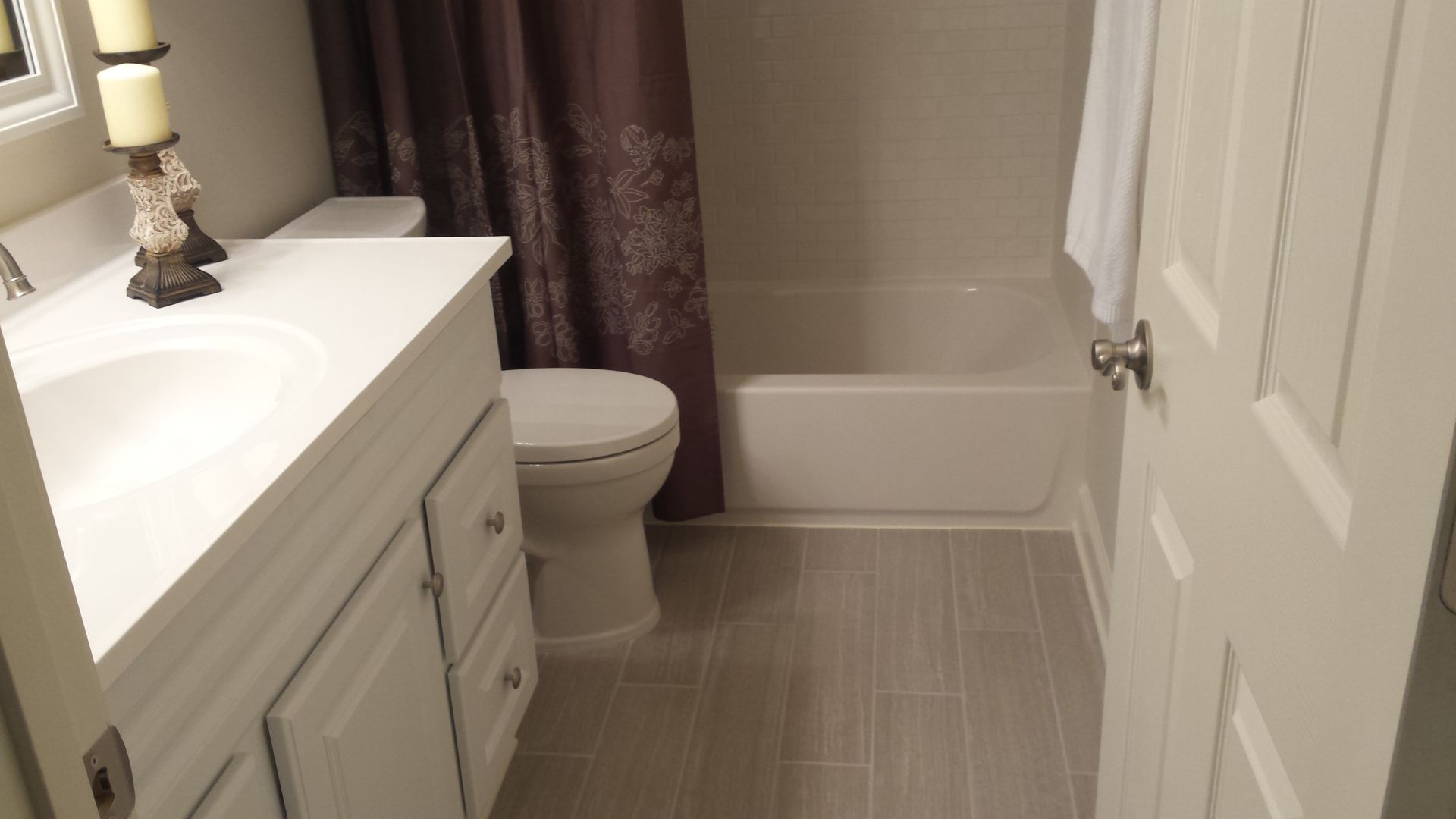 Small bathroom with white vanity, toilet, tub, and beige tile floor.