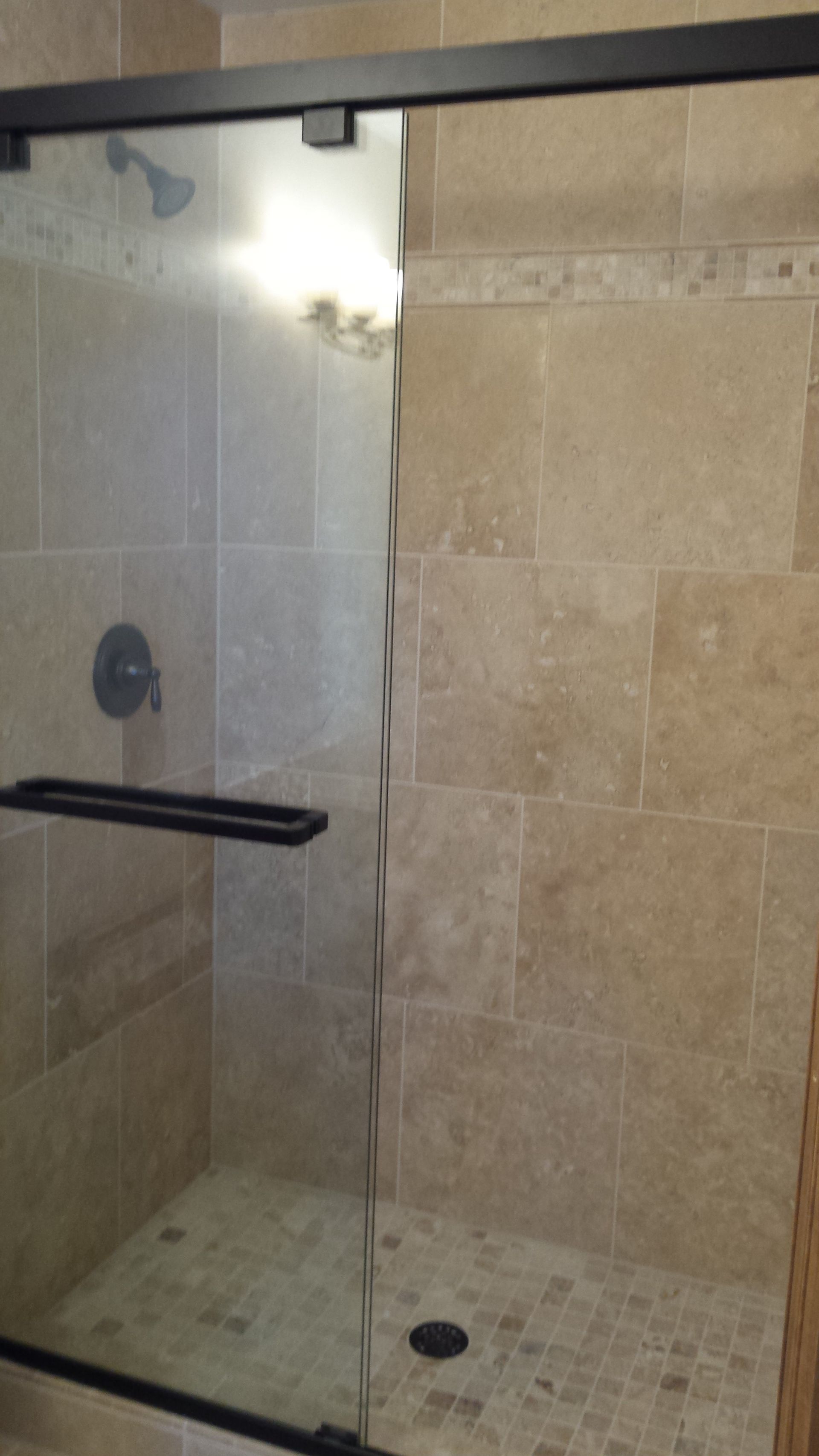 Glass shower with beige tile walls, black grab bar, and mosaic tile floor.