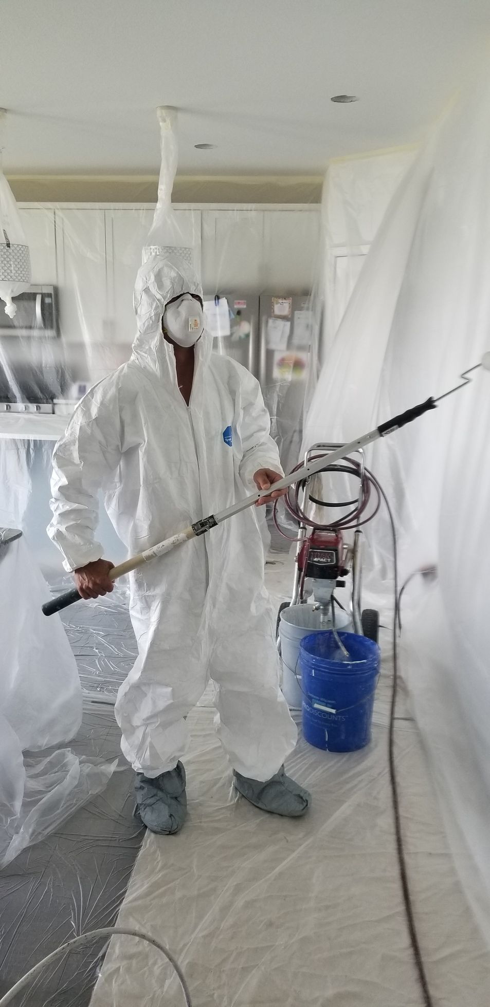 Worker in full protective suit spraying paint in a plastic-covered room