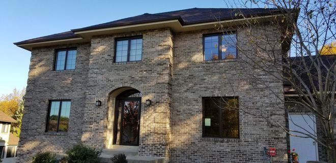 Stone two-story house with arched doorway and dark-framed windows in daylight