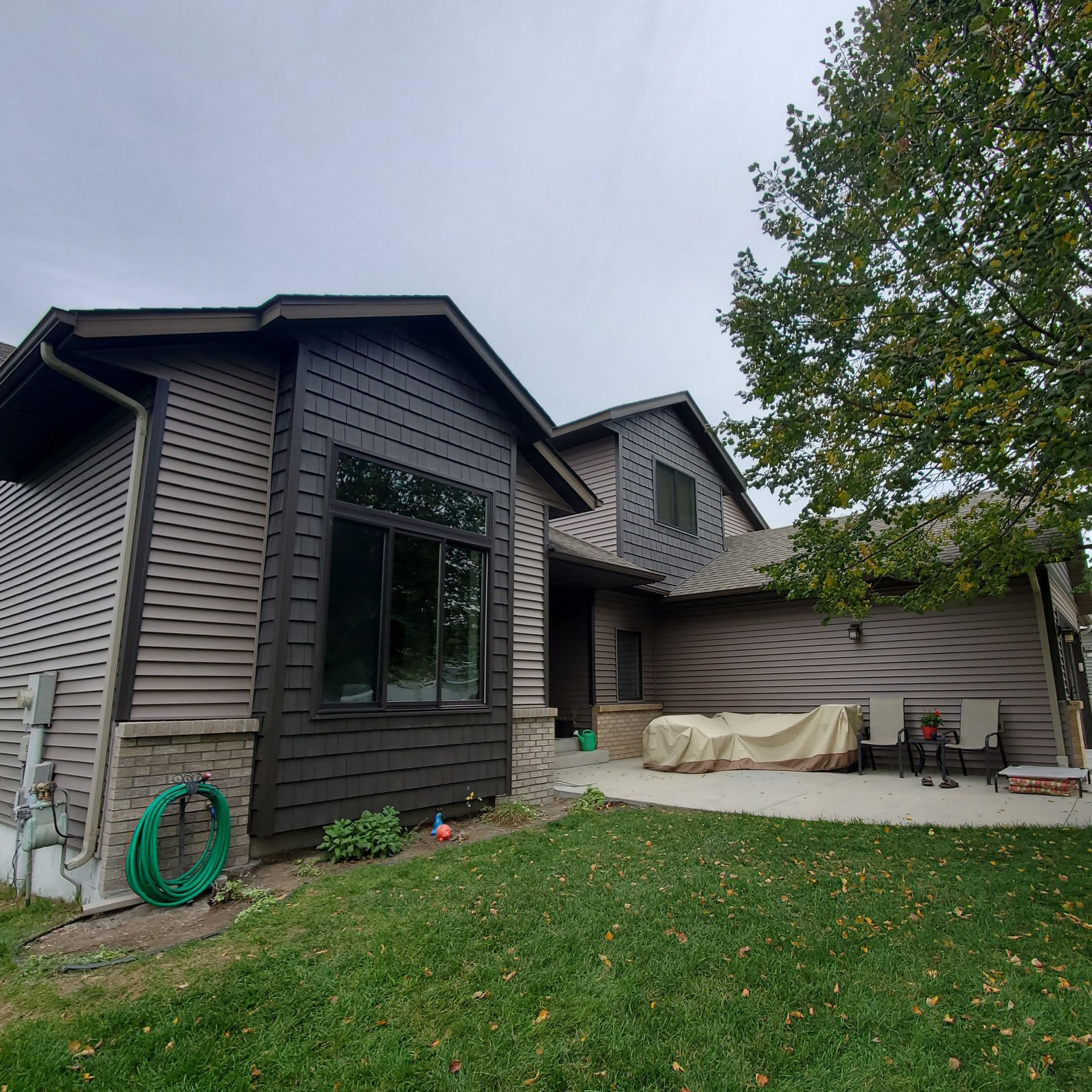 Exterior of a gray house with a green lawn, a large tree, and patio furniture under a covered area