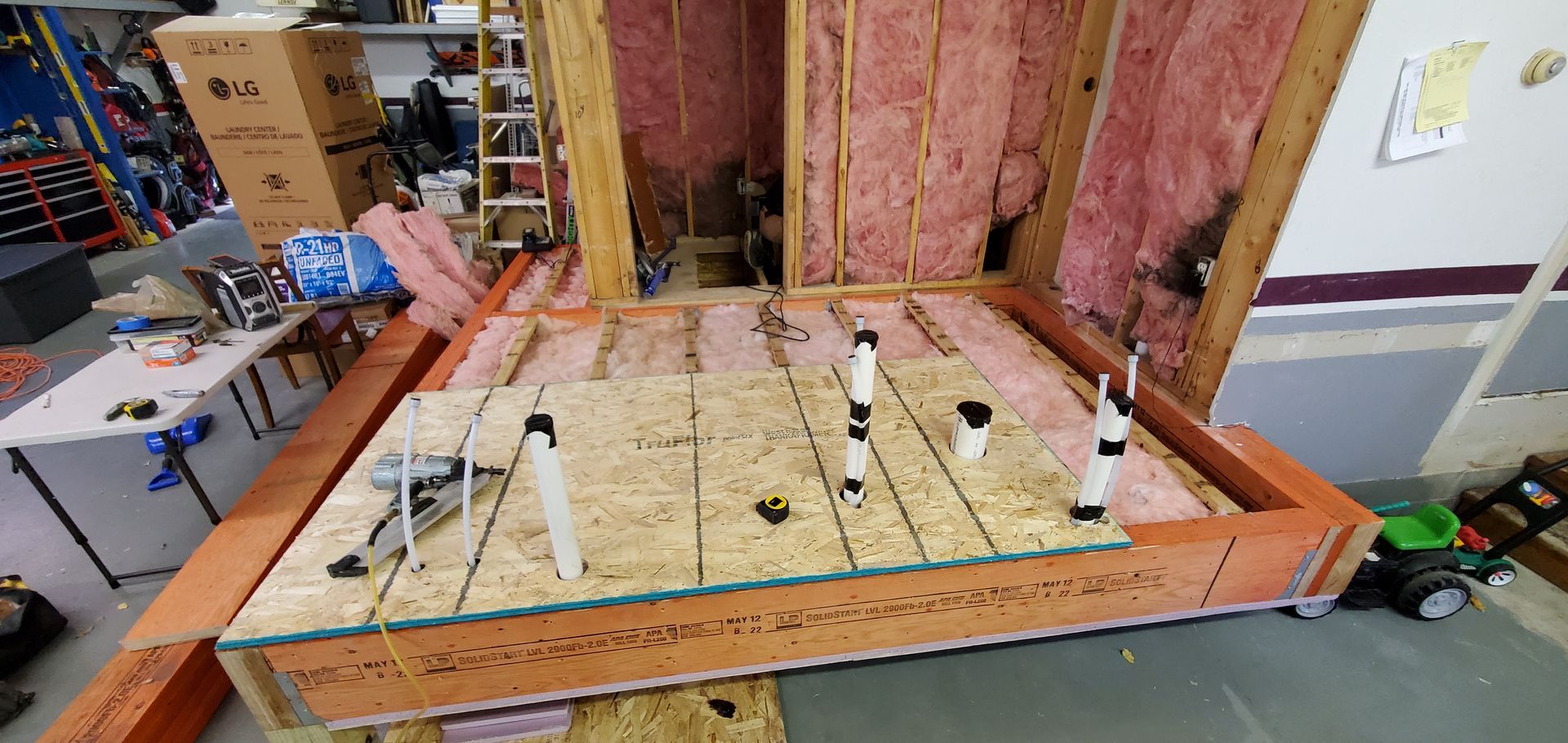 Framed basement floor with exposed insulation, plumbing pipes, and orange lumber around the perimeter