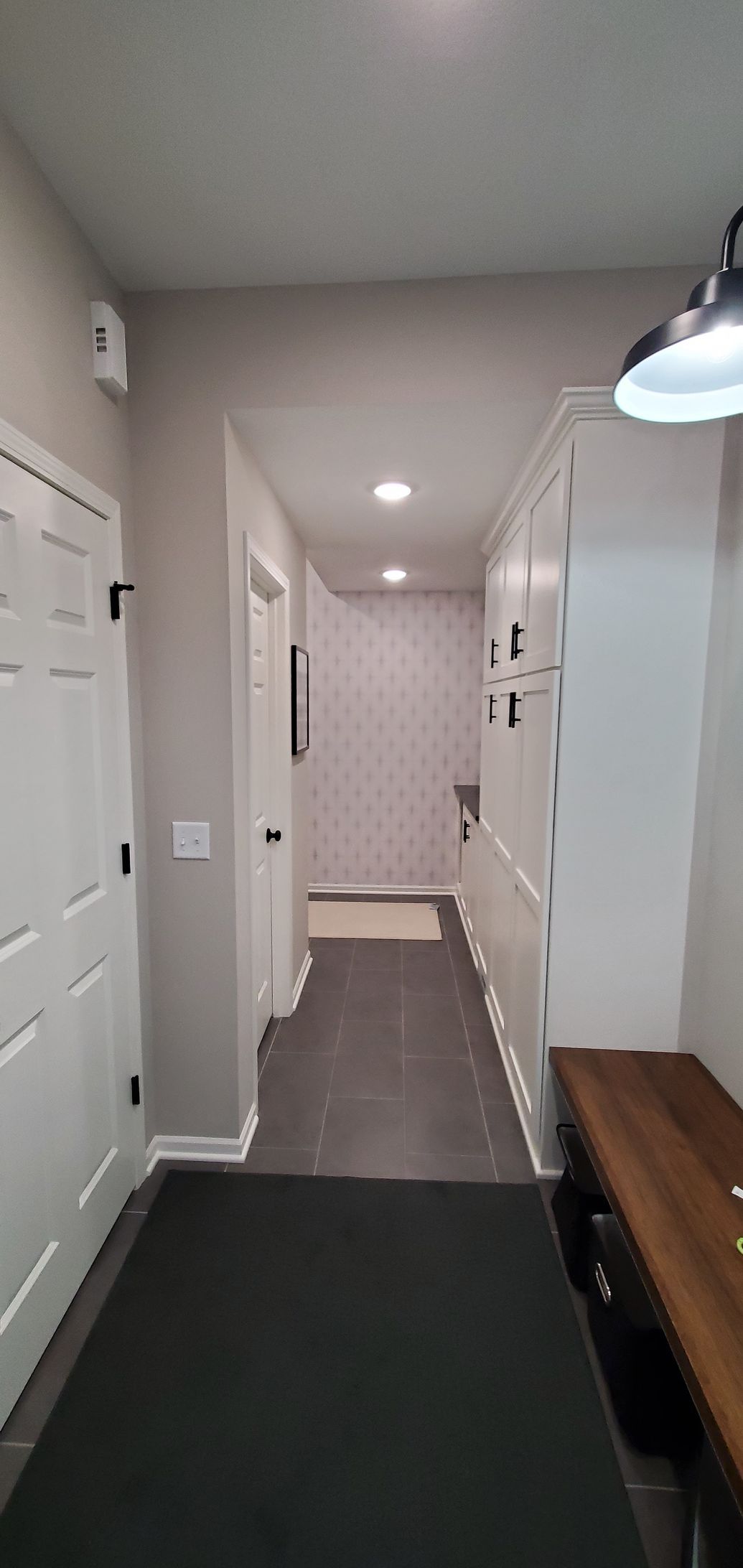 Narrow hallway with white doors, recessed lights, and a dark floor runner leading to a room.