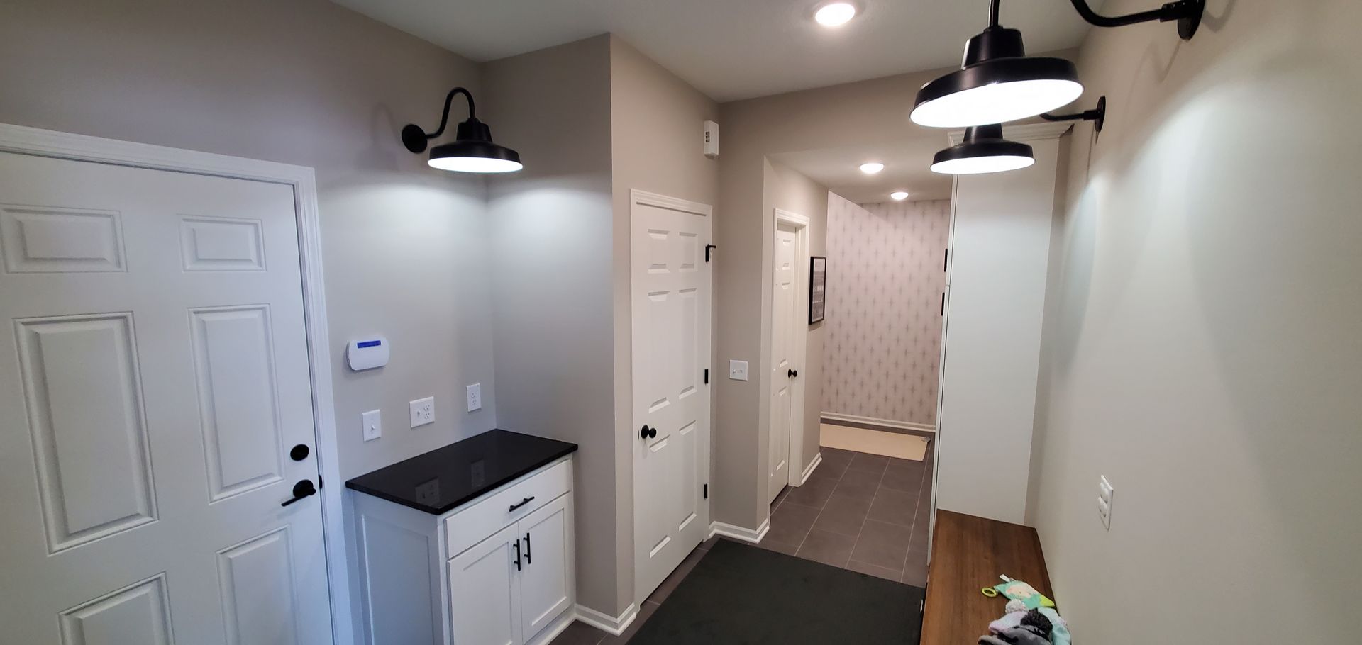 Modern hallway with white doors, gray walls, black wall sconces, and a small cabinet by the entrance