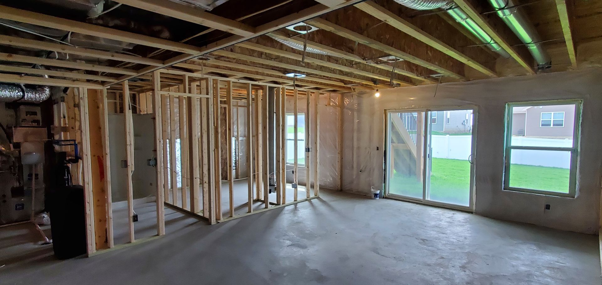 Partially finished basement with exposed studs, concrete floor, and sliding glass door to a backyard.