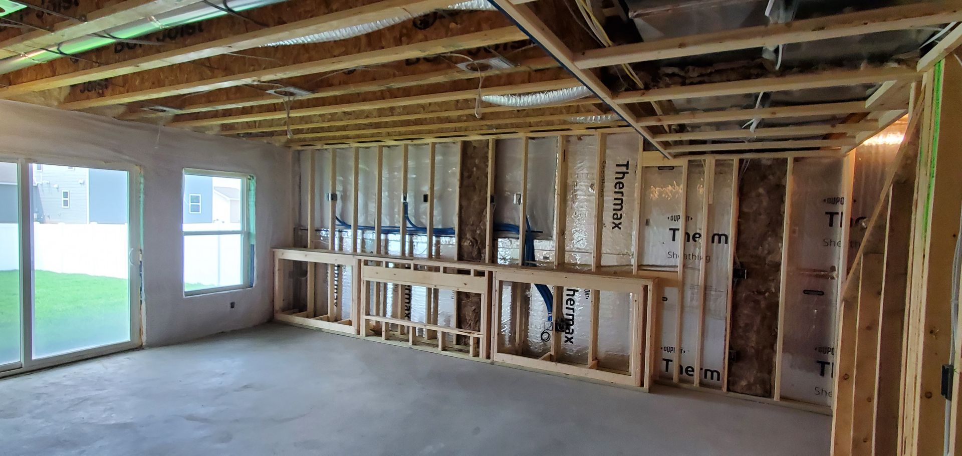 Unfinished room under construction with exposed wood framing, insulation, and windows letting in daylight