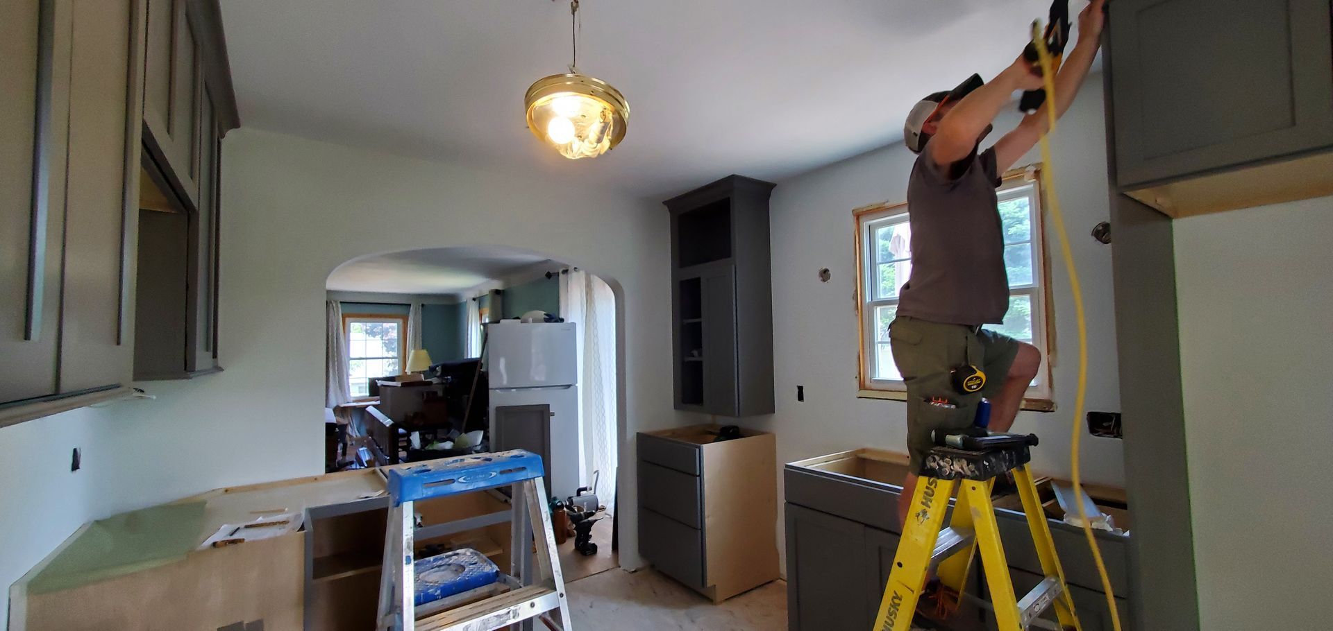 Worker on yellow ladder painting a kitchen ceiling in a partially renovated room.