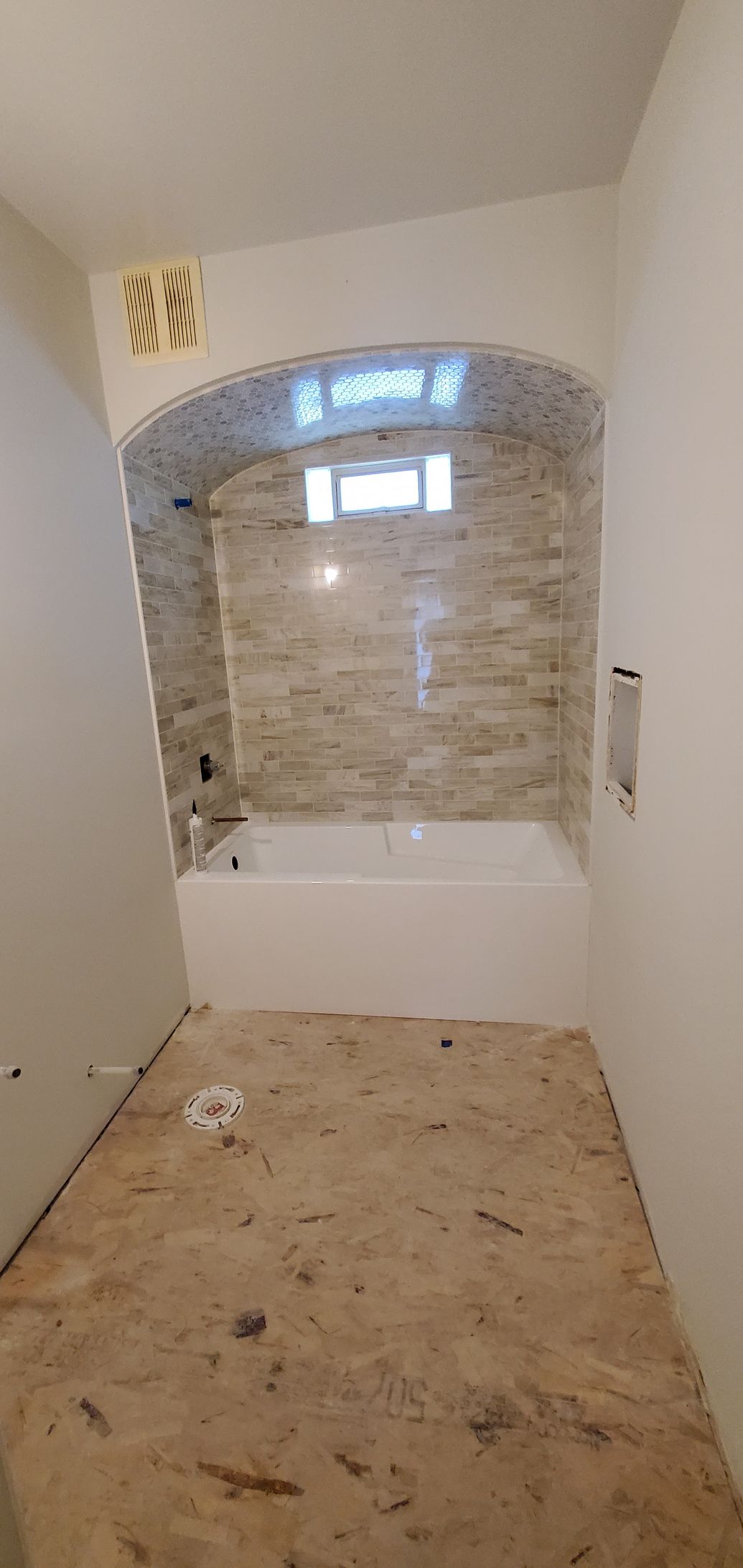 Bathroom under renovation with a tiled alcove bathtub and unfinished floor.
