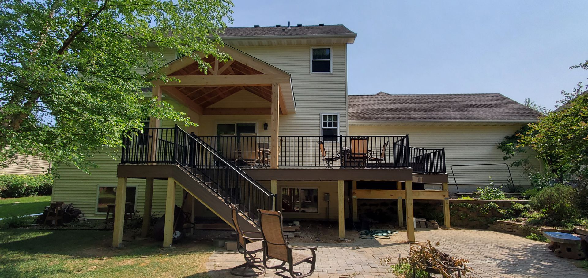 Backyard house with raised deck, stairs, and patio seating under a large tree