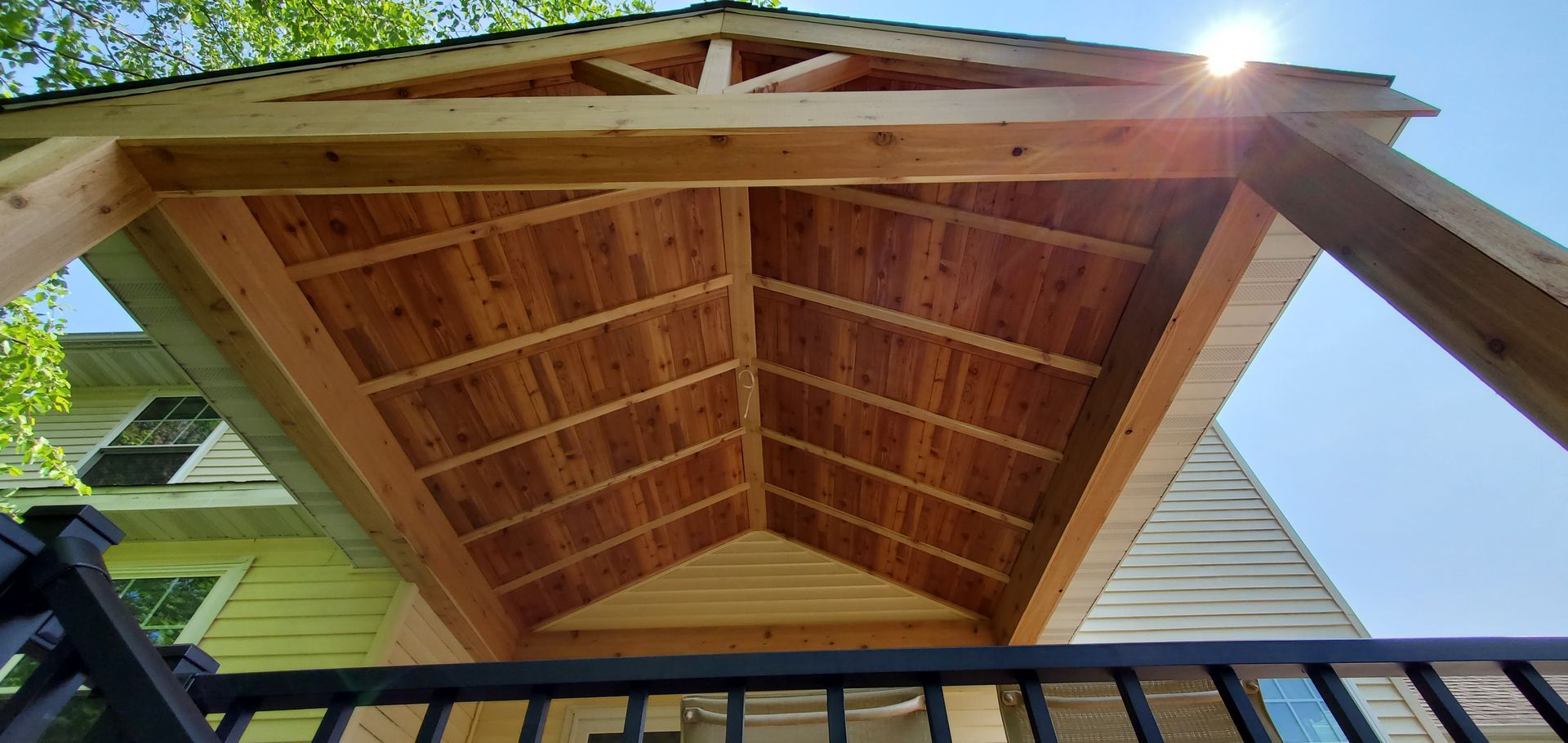 Underside of a wooden gable roof over a balcony, with sunlight at the peak