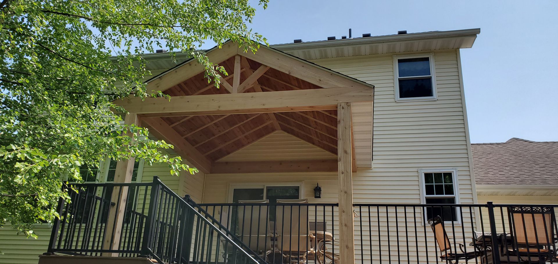 House with a covered porch, wooden truss roof, and black metal railing in bright daylight
