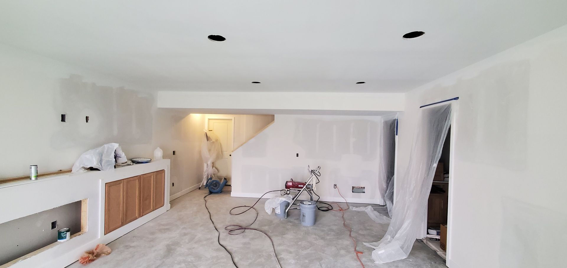 Bright living room renovation with white walls, exposed floor, and plastic-covered doorway