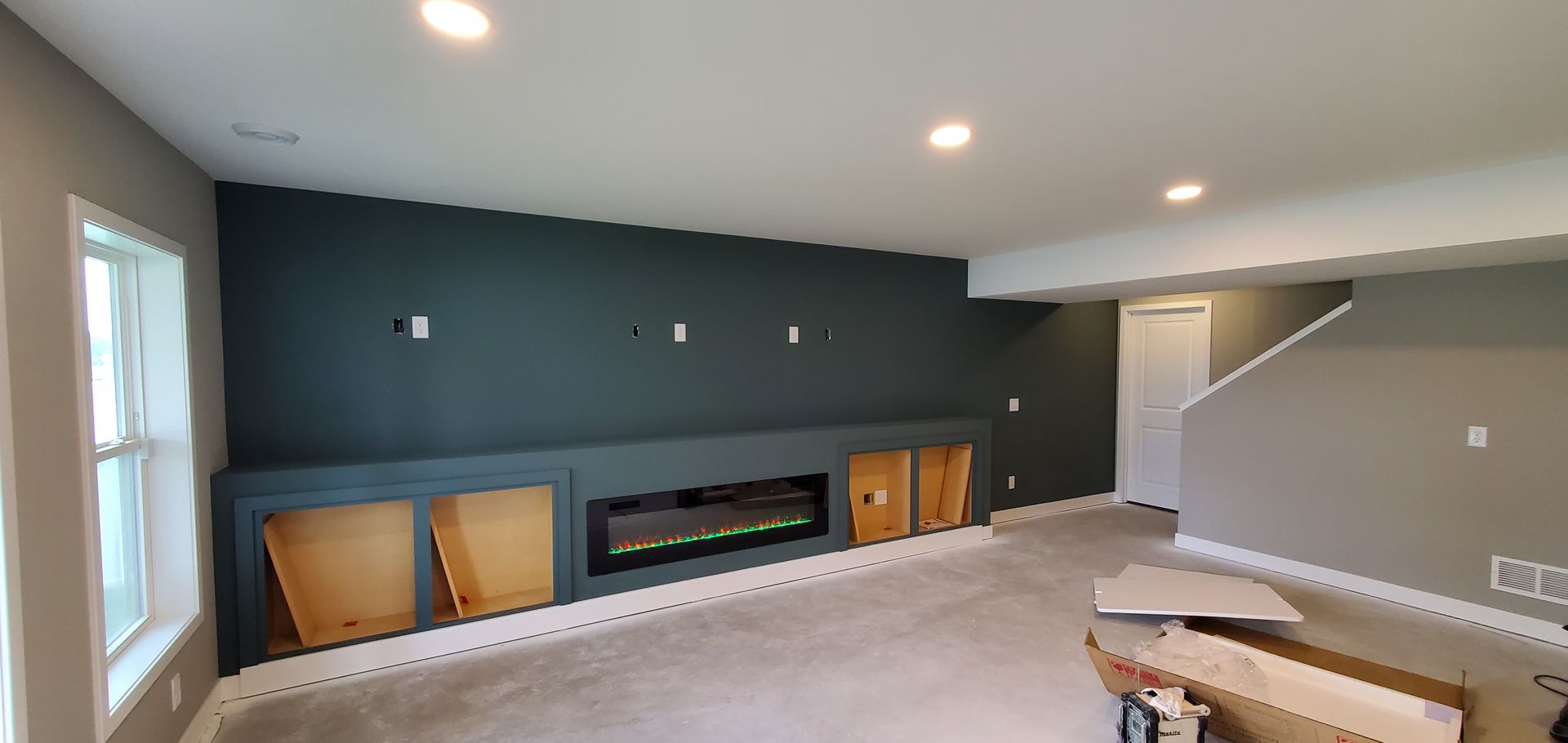 Empty living room with dark green accent wall, fireplace, windows, and a stairway to the right