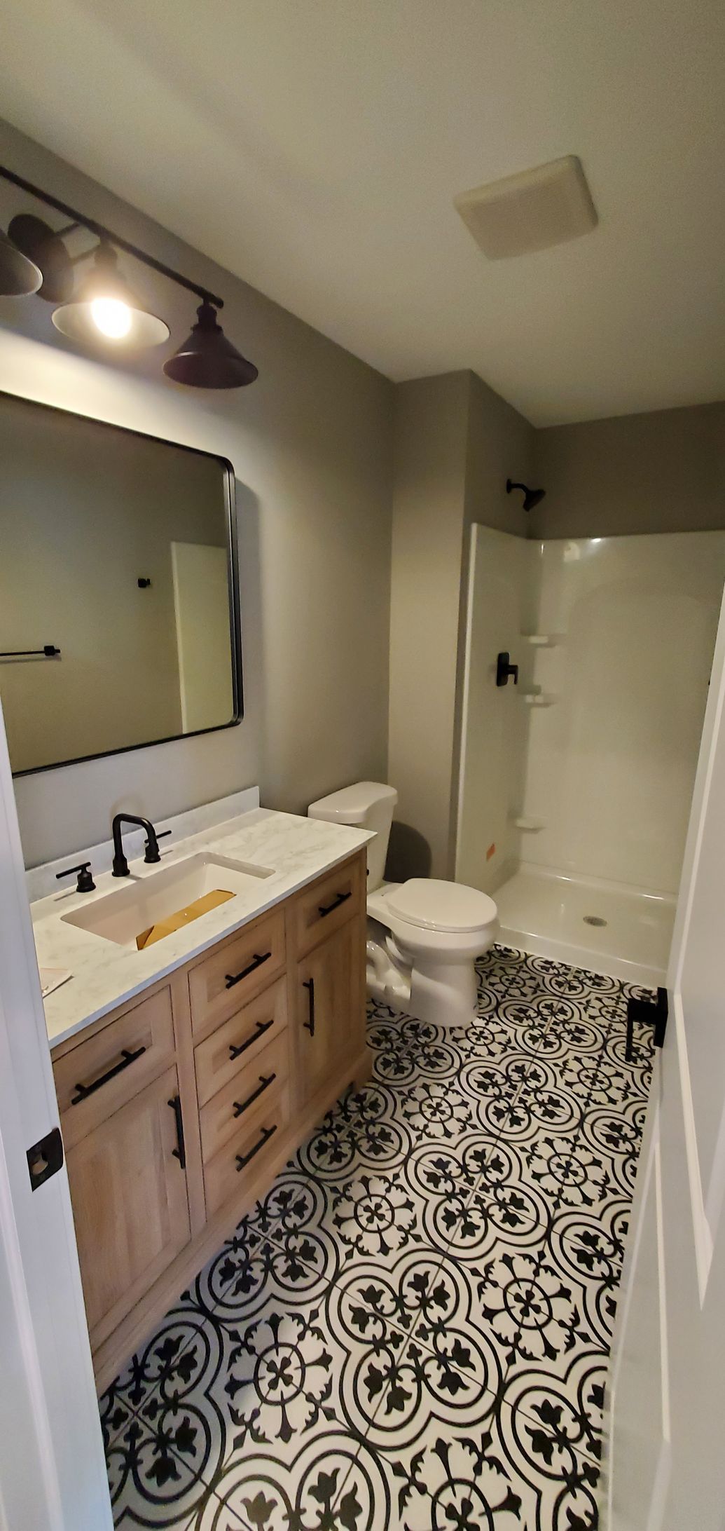 Bathroom with wood vanity, large mirror, toilet, and black-and-white patterned tile floor.