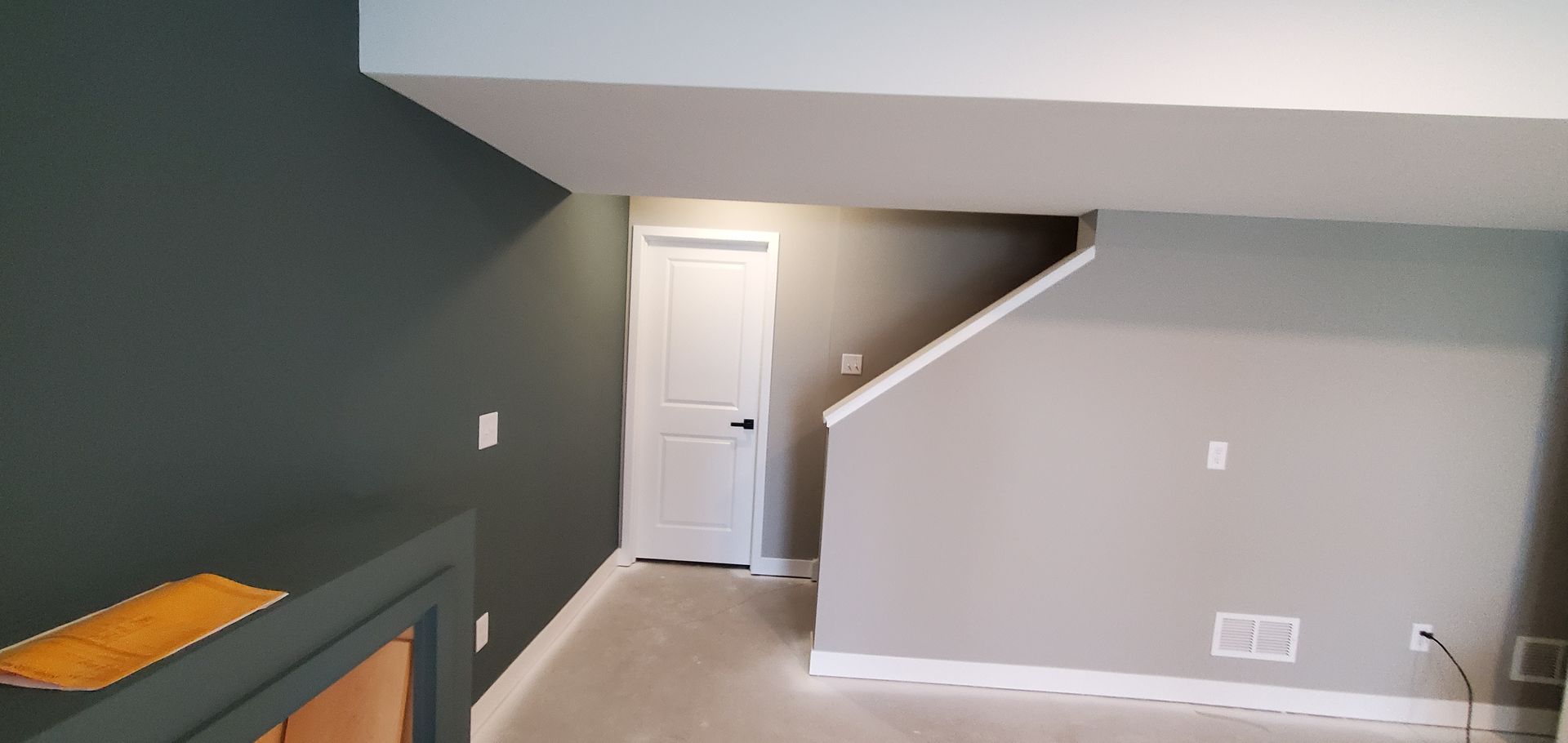 Empty gray carpeted room with white trim, a doorway, and stairs along the right wall.