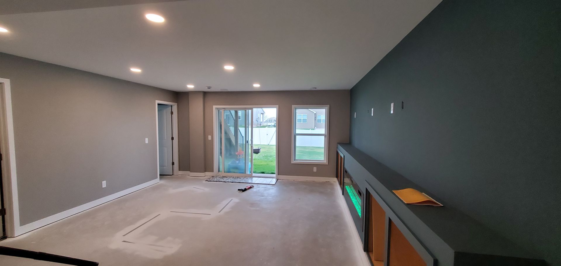 Empty gray living room with carpet, sliding glass doors, and a dark accent wall