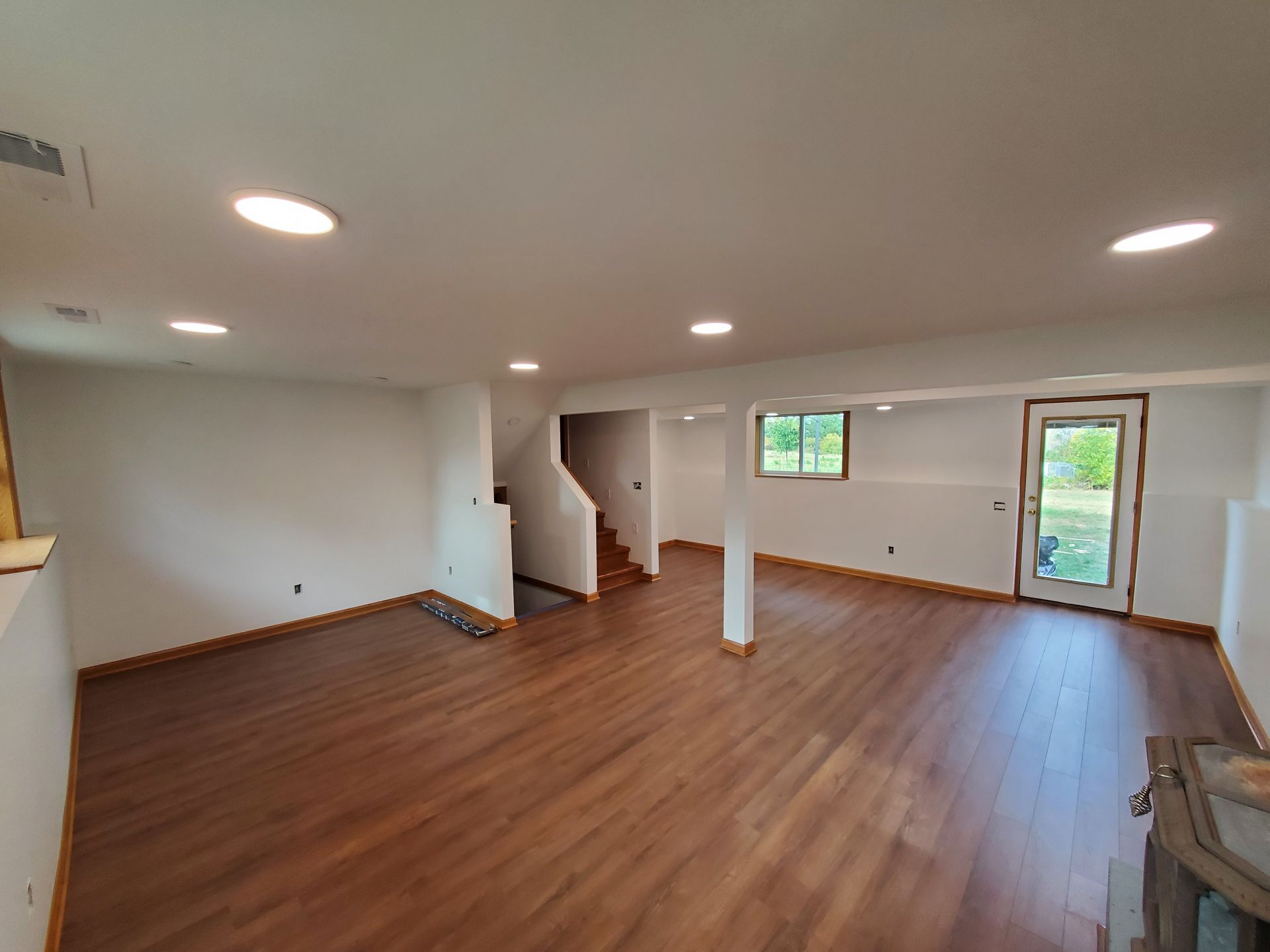 Empty open-plan living room with wood floors, white walls, recessed lights, and sliding glass door to outside