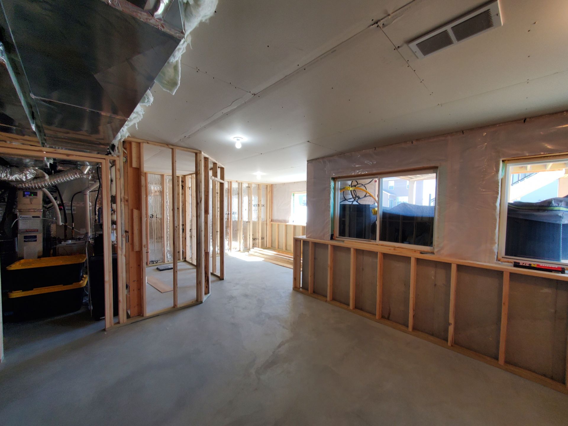 Unfinished interior of a building with exposed framing, concrete floor, and large windows letting in daylight