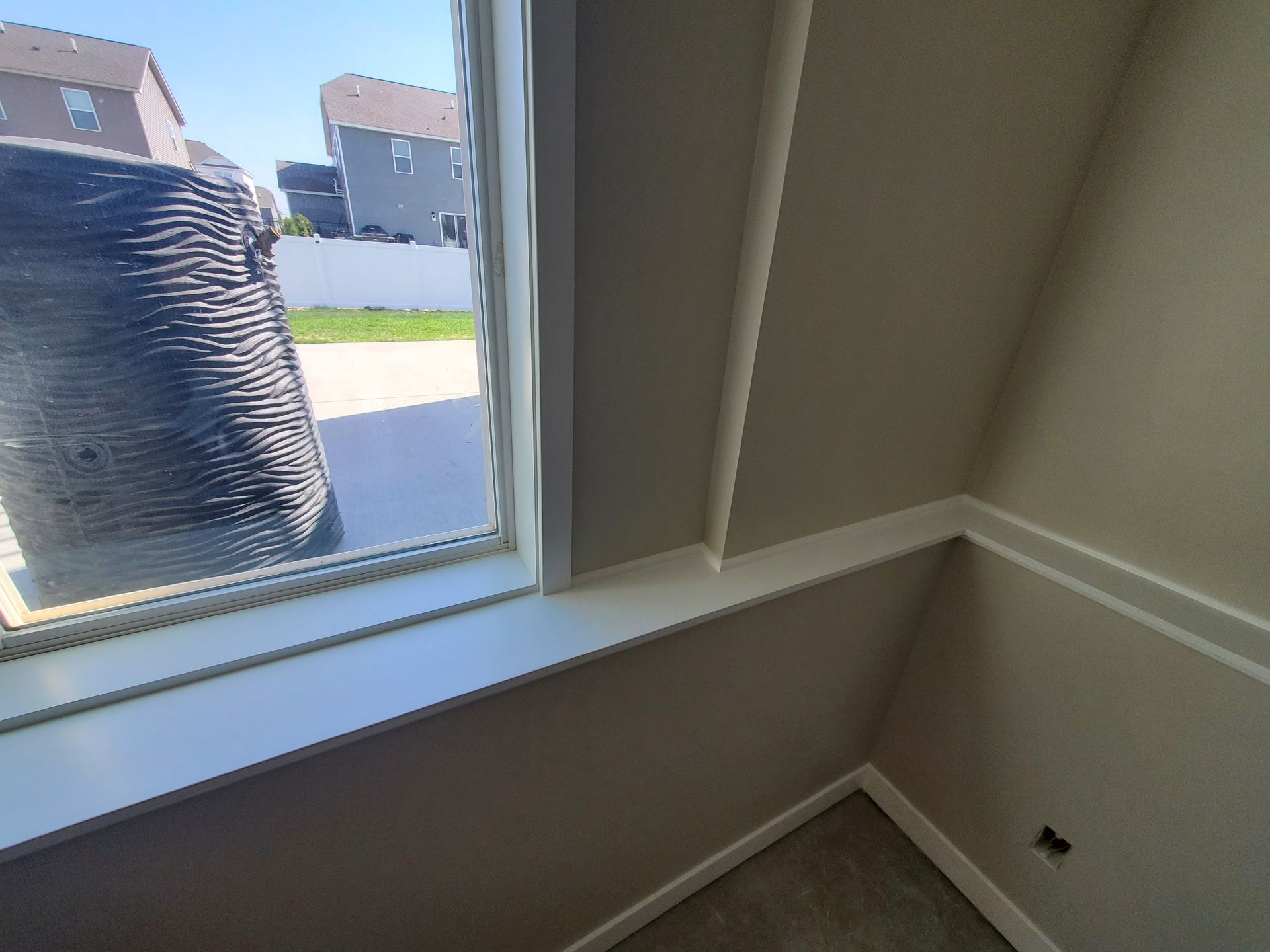 Empty room corner with a large window, beige walls, and white trim overlooking a driveway and street.