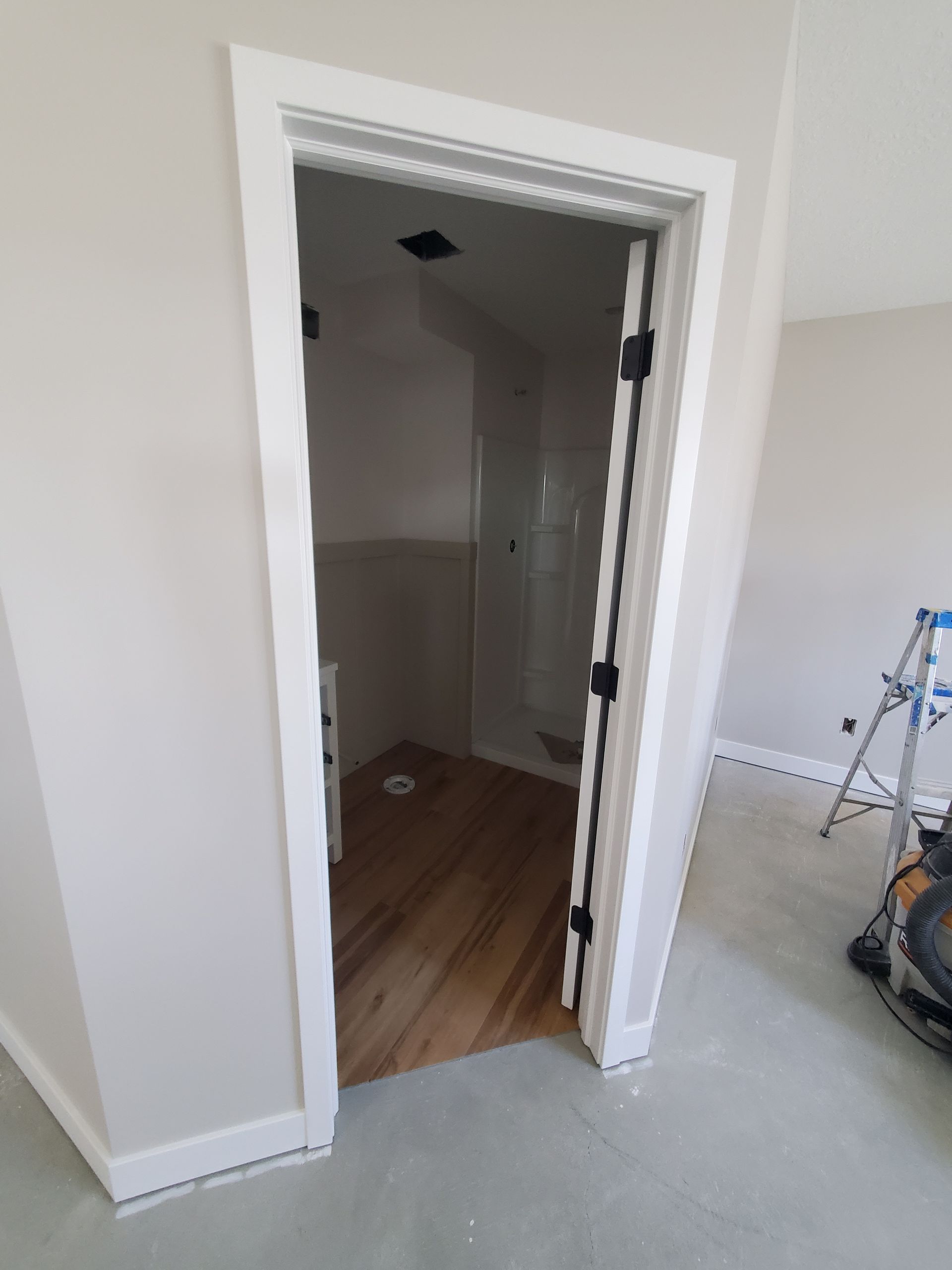 Open doorway to a small closet or hallway with wood floor, white trim, and unfinished room walls