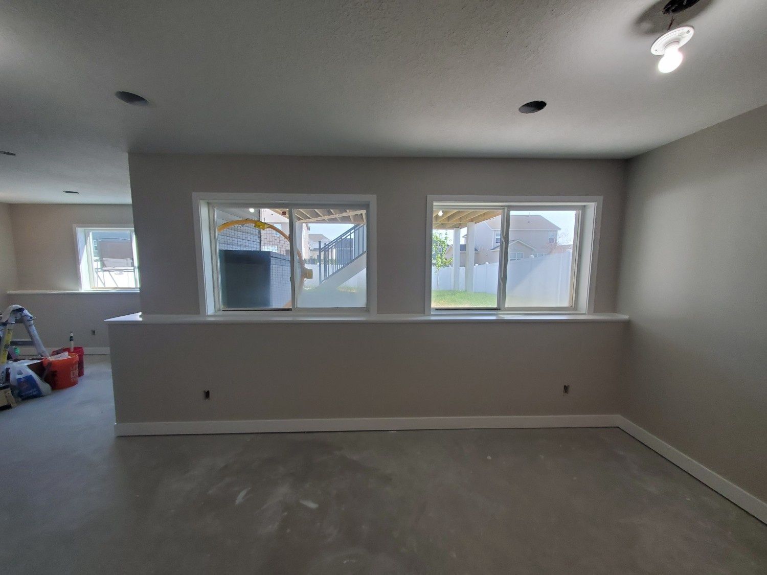 Empty gray room with three windows, carpeted floor, and ceiling lights