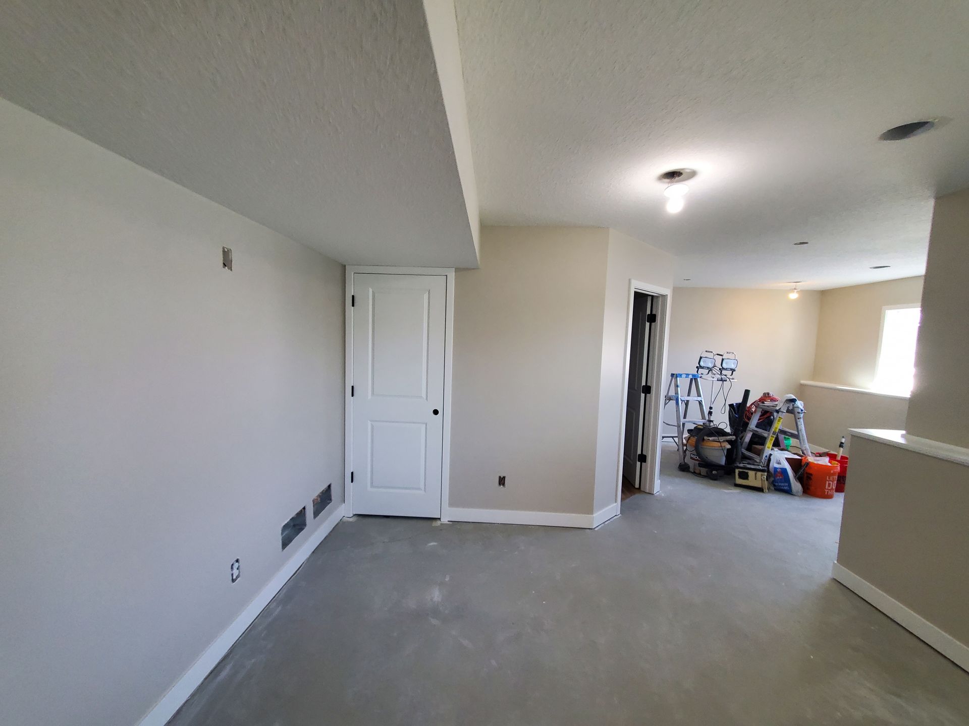 Empty carpeted room with white walls, closet doors, and a hallway opening to cluttered boxes and tools.