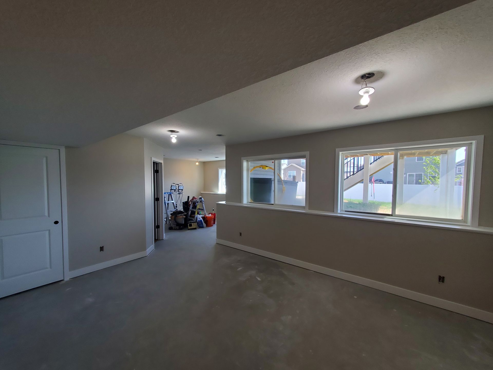 Empty living room with carpet, beige walls, recessed lights, and large windows overlooking a yard