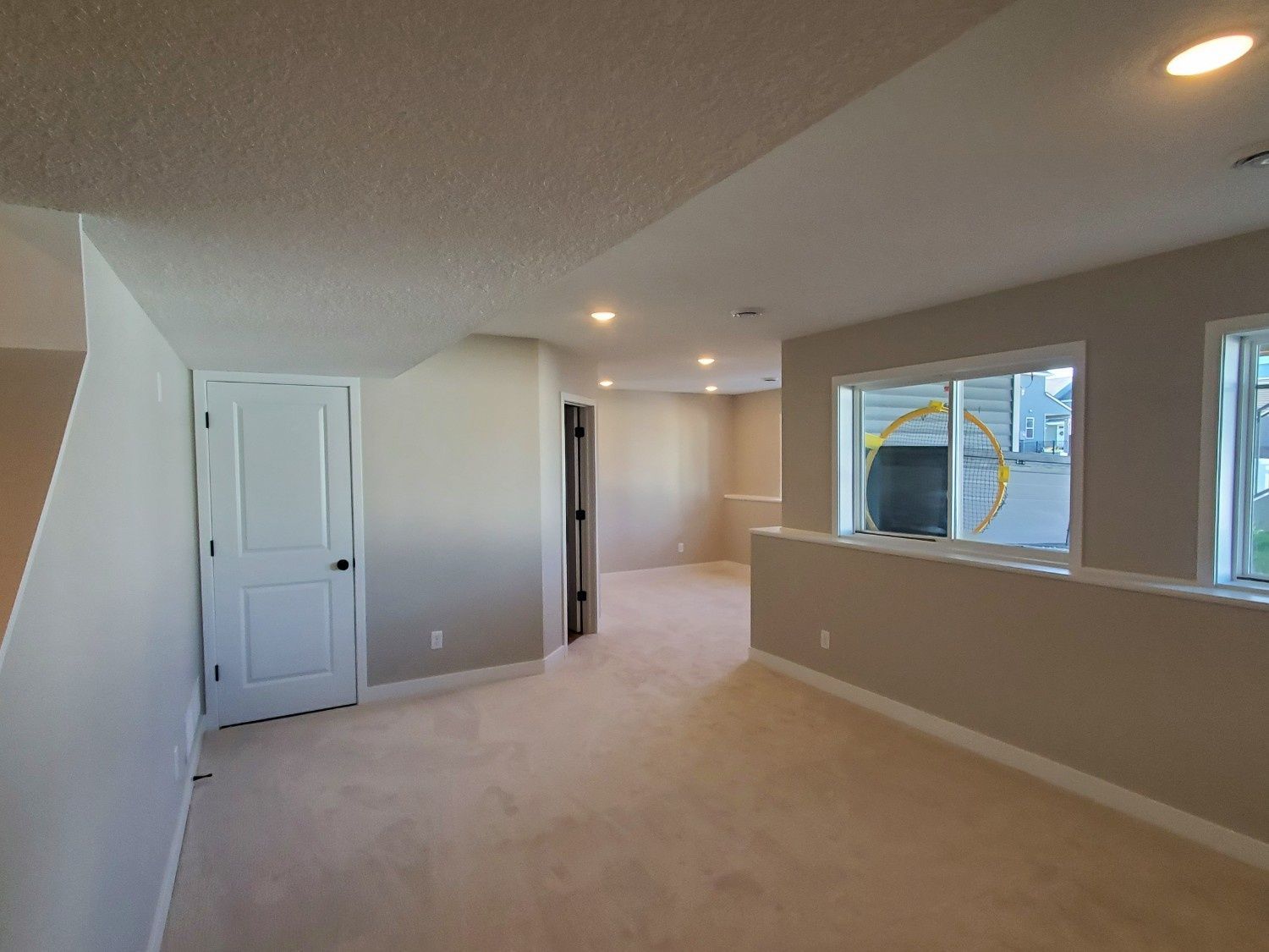 Empty beige hallway and living area with white doors, windows, and recessed ceiling lights