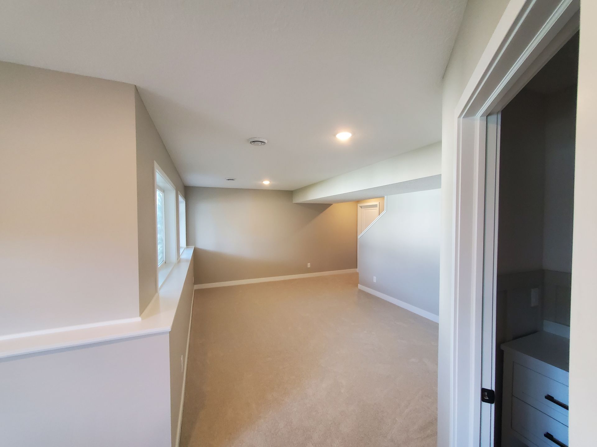 Empty beige carpeted room with recessed lights, white trim, and an open doorway on the right
