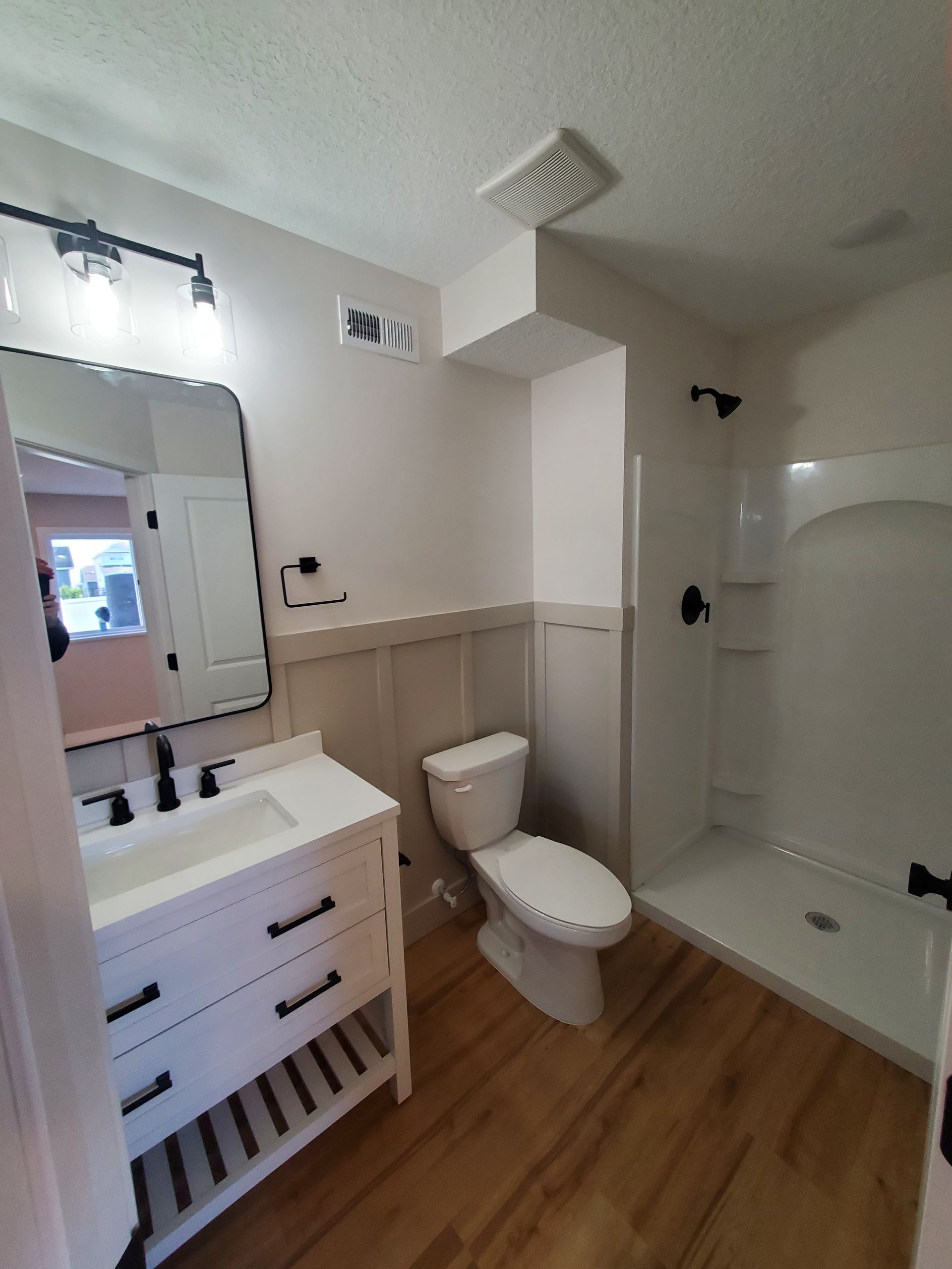 Bathroom with white vanity, toilet, and shower/tub combo, featuring beige walls and wood-look flooring