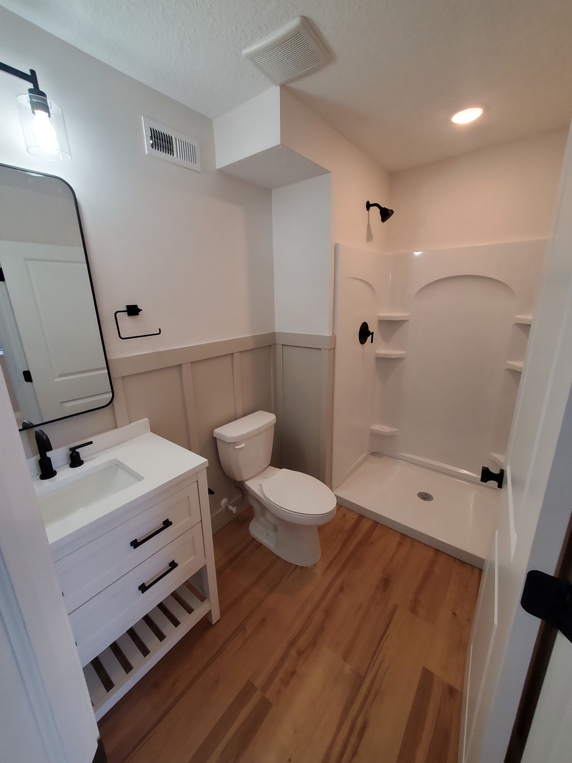 Small white bathroom with wood floor, vanity, toilet, and walk-in shower.