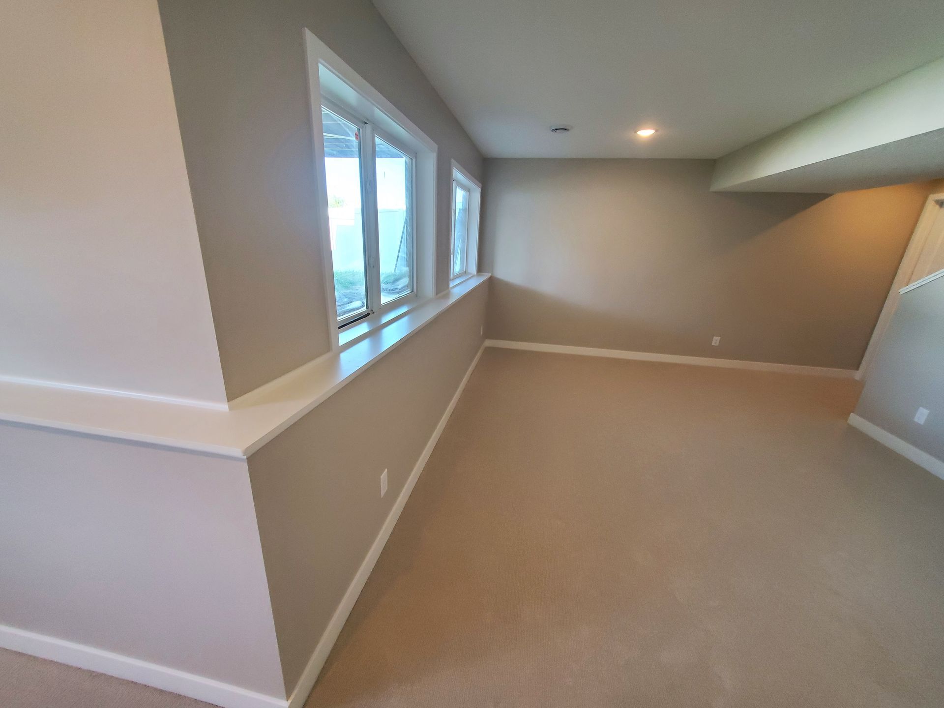 Empty beige room with large windows and recessed ceiling lights
