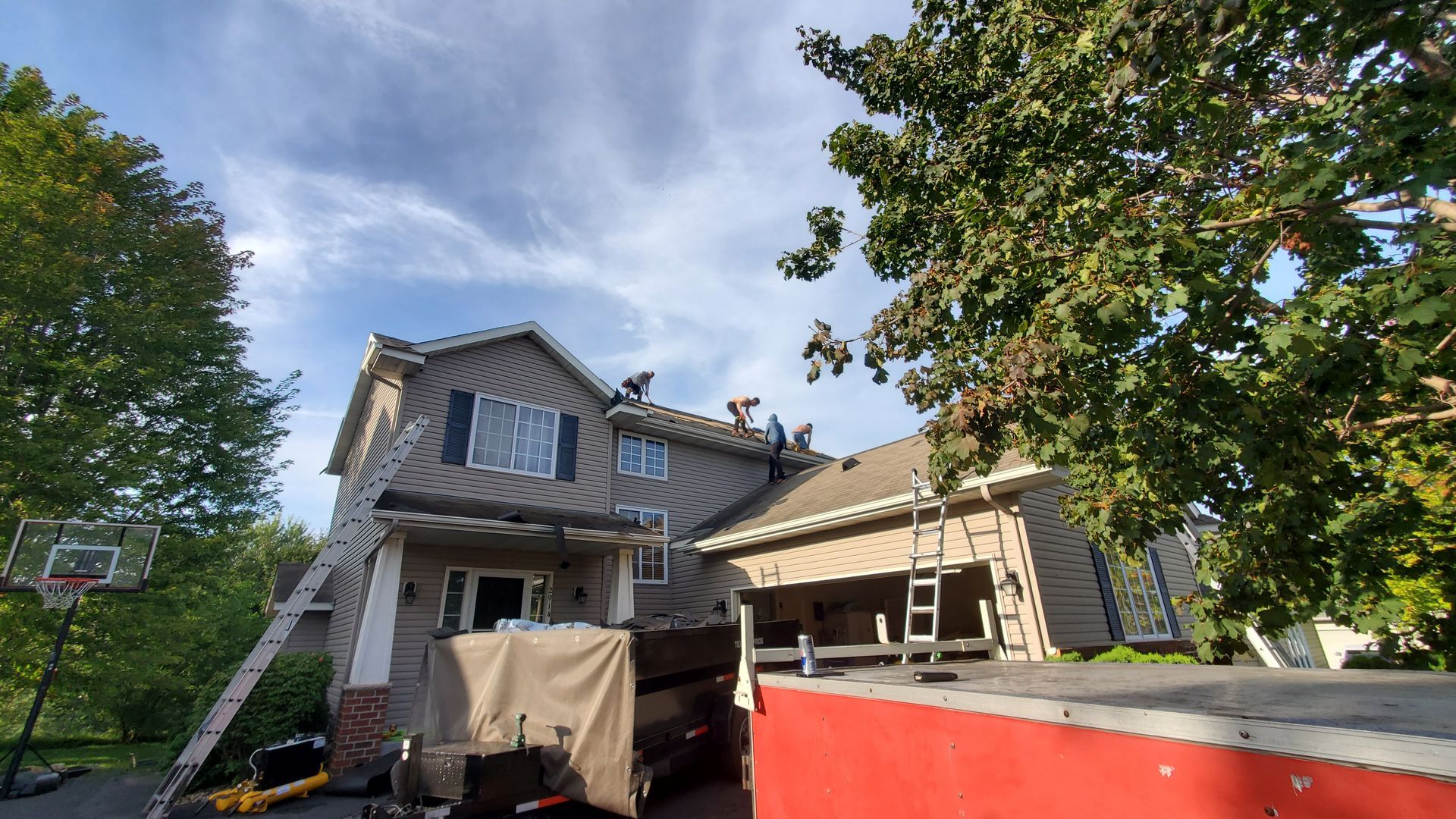 Two-story house under renovation with scaffolding, tarp, and a red dumpster in the foreground