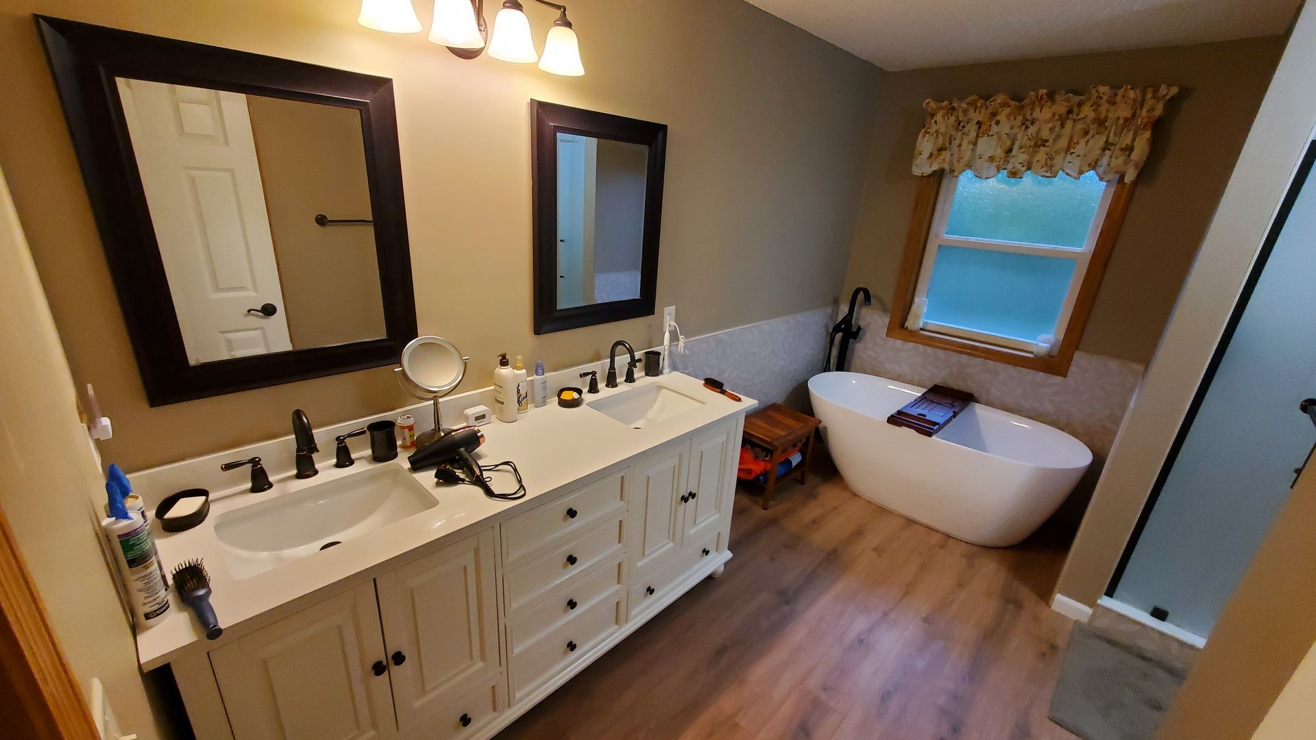 Modern bathroom with double vanity, mirror, freestanding tub, and wood-look floor.