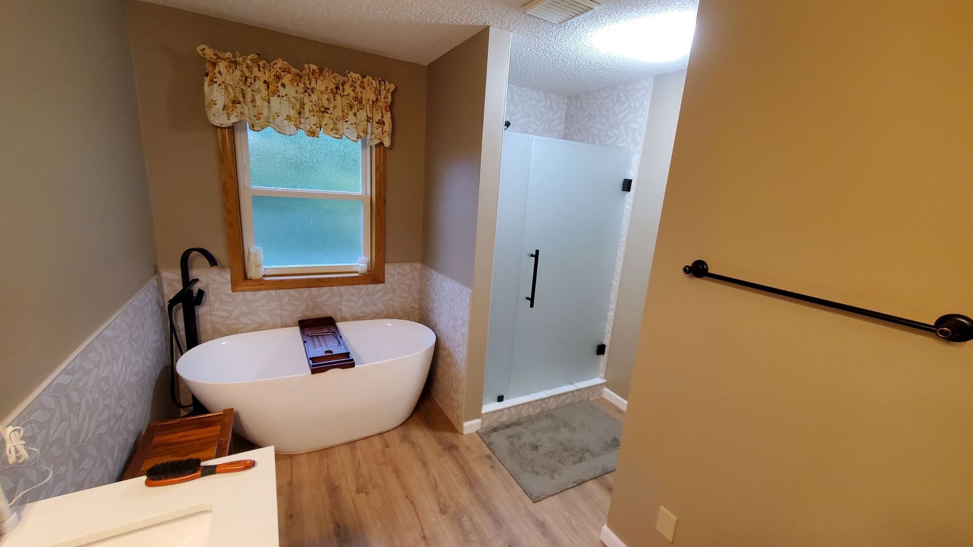 Small bathroom with a freestanding tub, shower, and window with a valance, finished in beige and wood tones