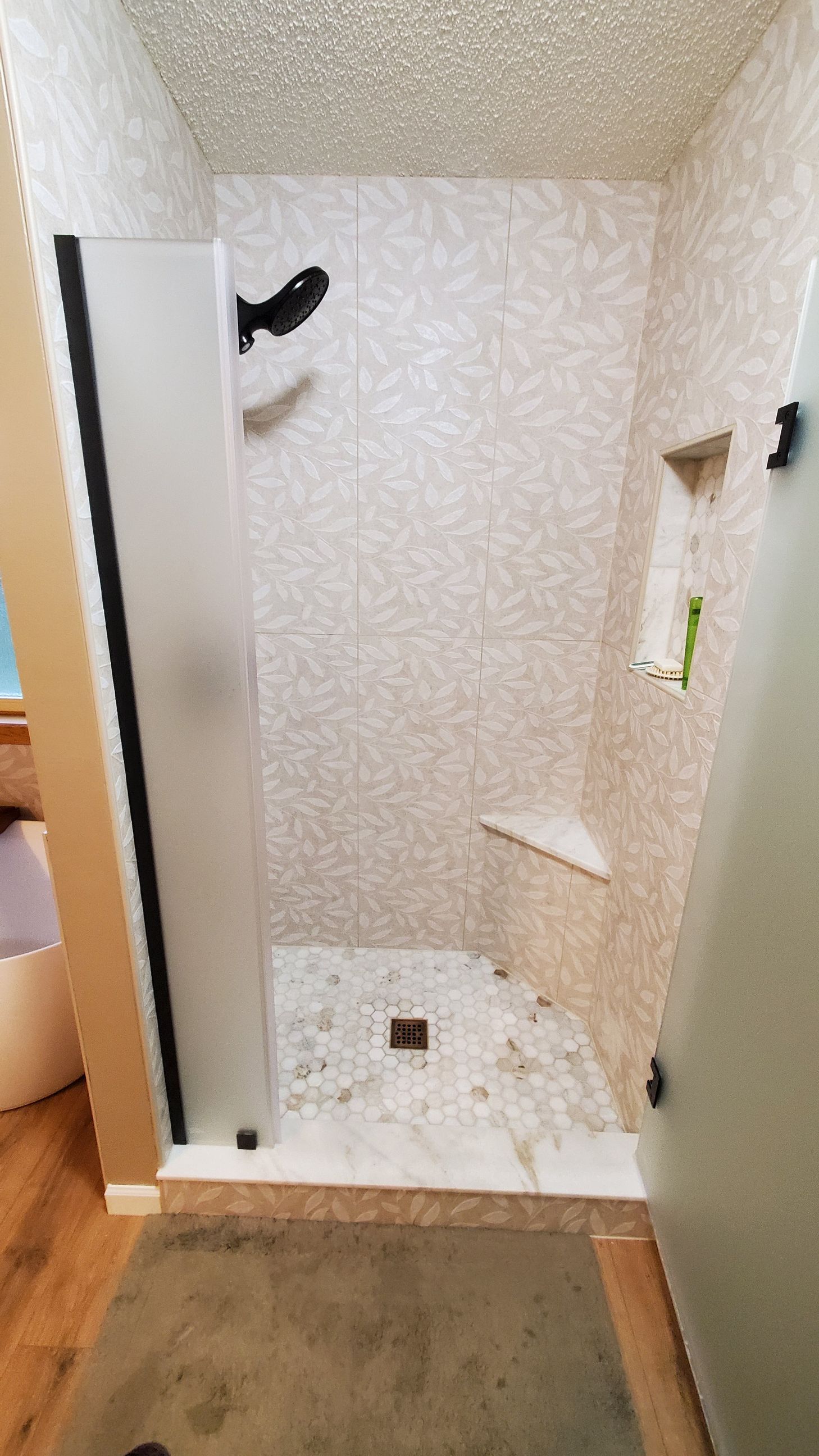Small tiled shower stall with white walls, black fixtures, and a built-in corner shelf.