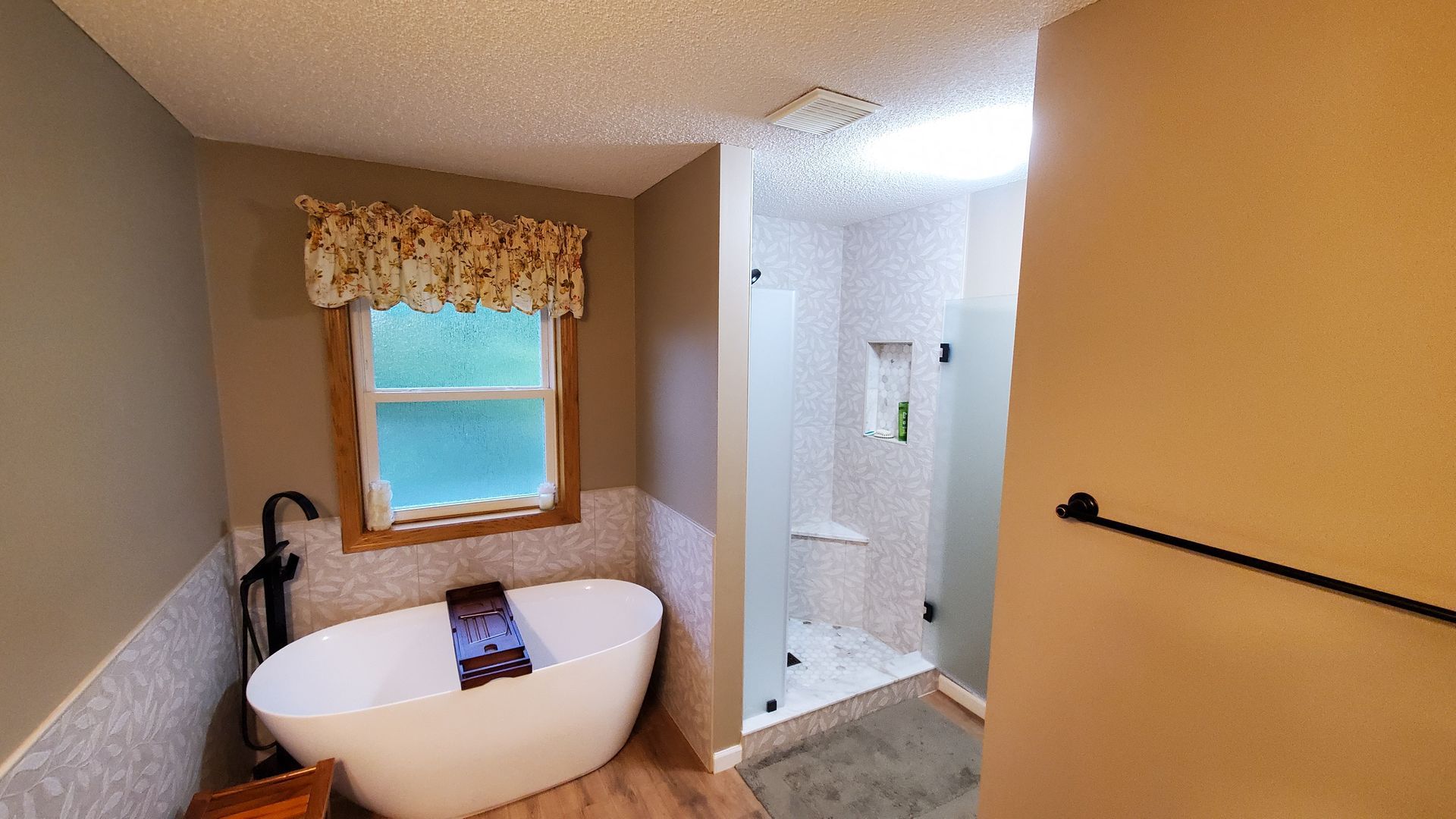 Small bathroom with a white freestanding tub, window, and adjoining glass shower.