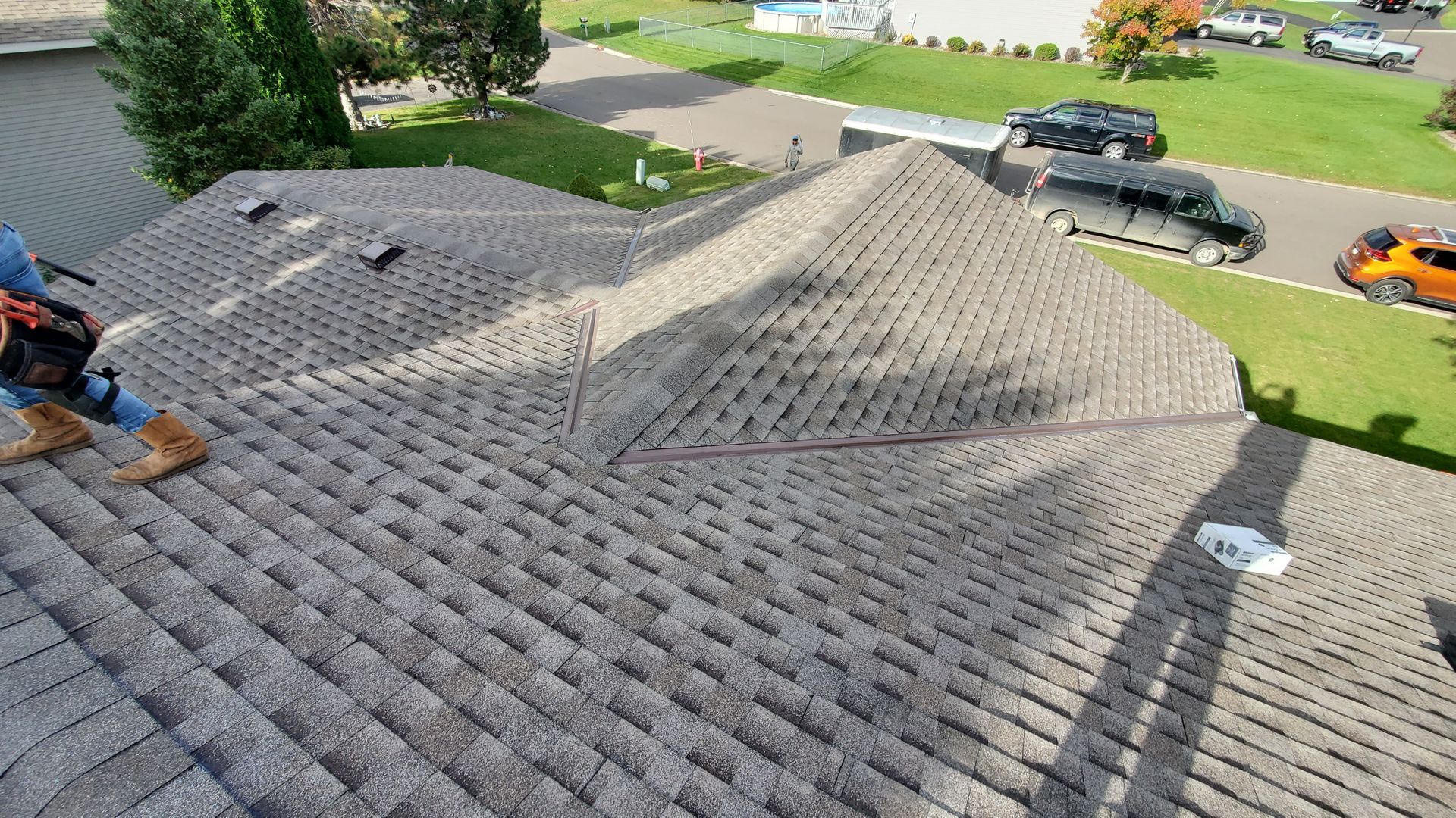 Workers repairing a gray shingle roof, with tools and materials on the rooftop and houses below.
