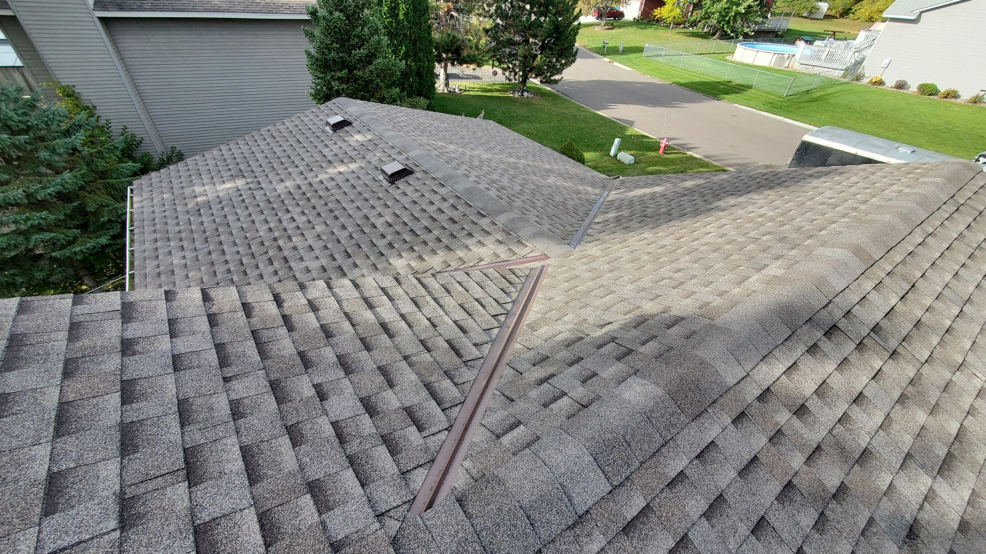 Damaged shingled roof with a visible ridge line and neighboring houses in the background