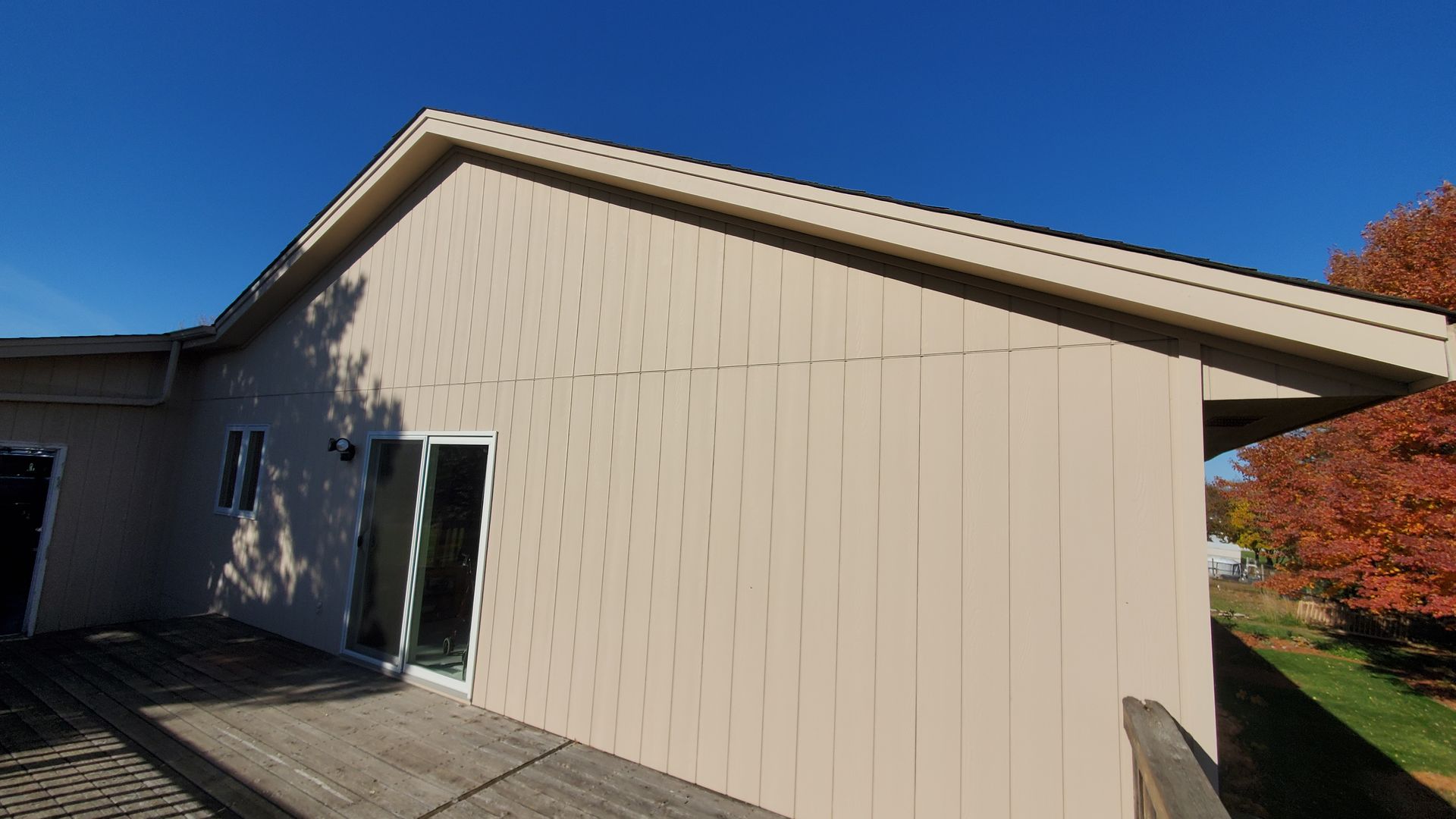 Beige house exterior with a sloped roof, sliding glass door, and clear blue sky.