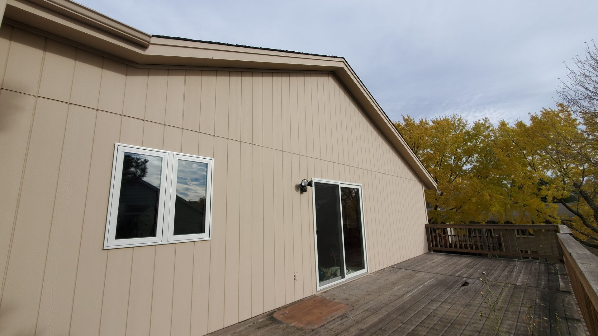 Beige house exterior with two windows and a deck beside autumn trees